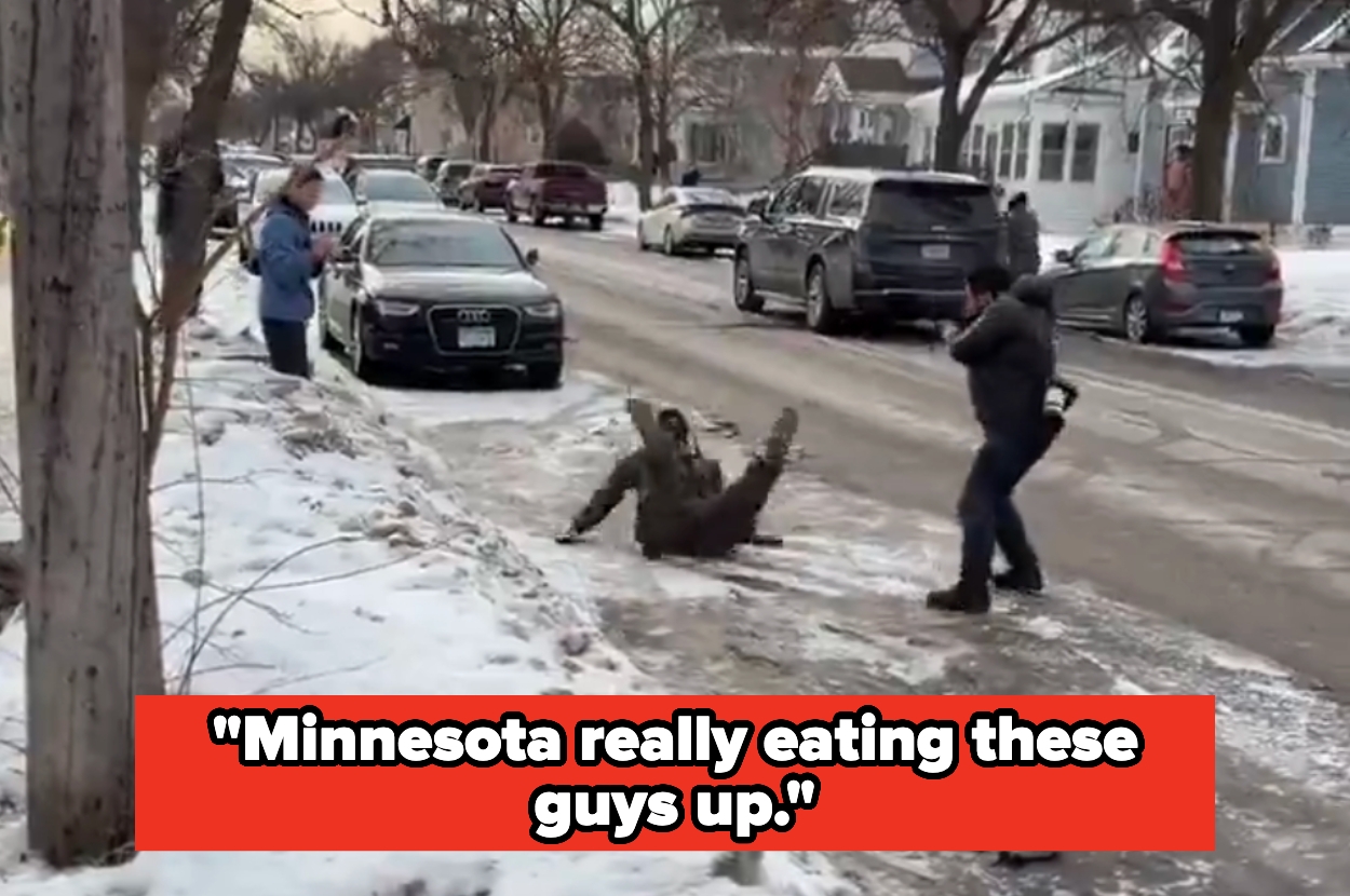 Person slips on icy street while two people nearby are filming, with snowy neighborhood in the background. Text overlay reads: “Minnesota really eating these guys up.”