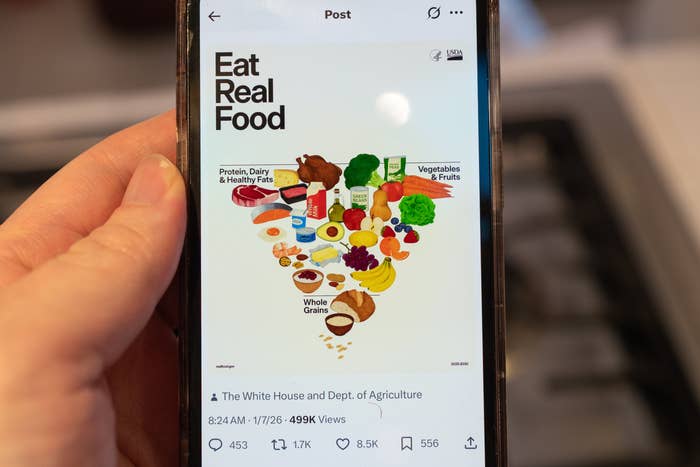 Hand holding a telephone  showing a tweet from The White House and Dept. of Agriculture promoting "Eat Real Food" with nutrient  graphics