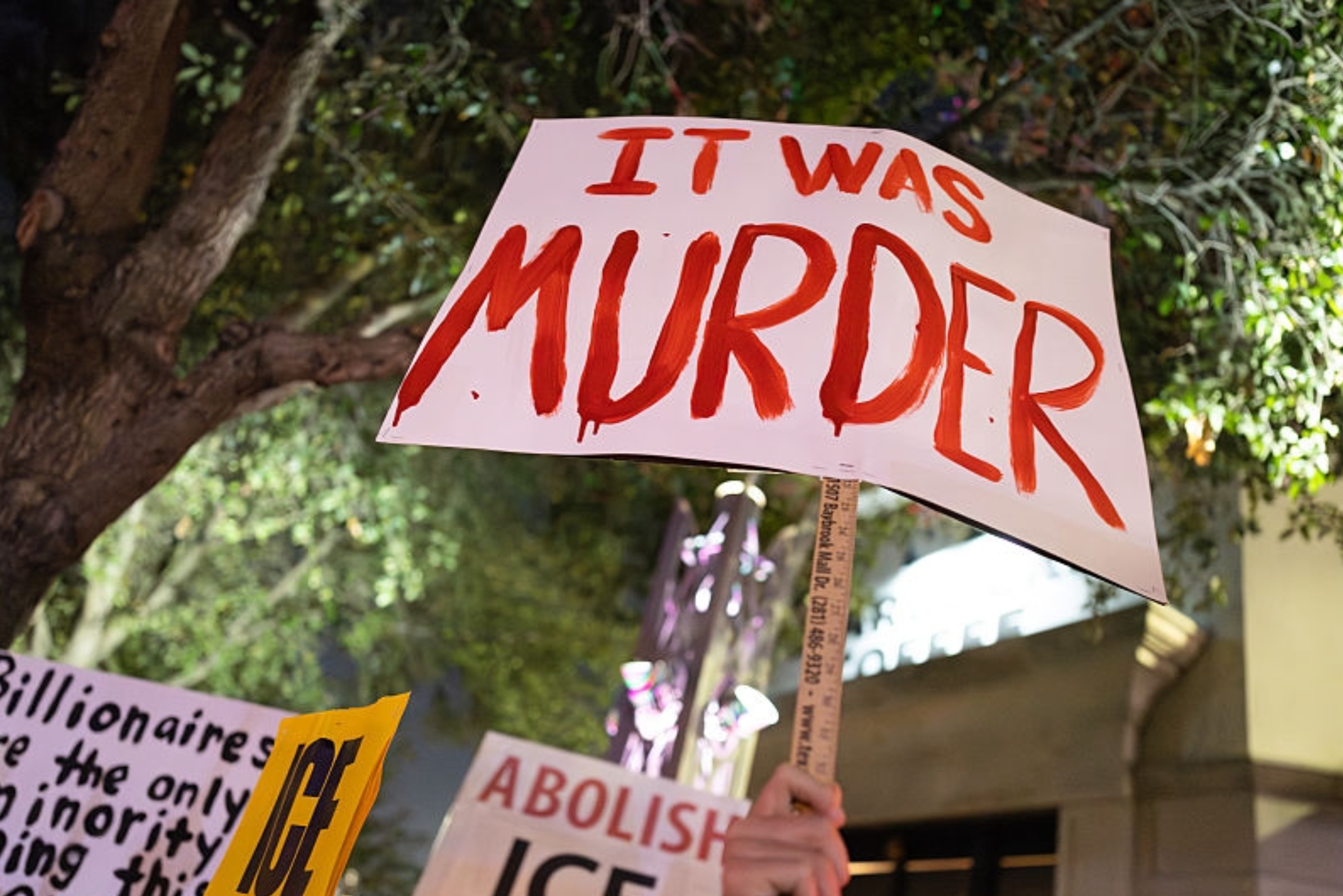 Demonstranter holder skilt med teksten «DET VAR DRAP»; "ABOLISH ICE," og en kritikk av milliardærer ved en nattlig demonstrasjon