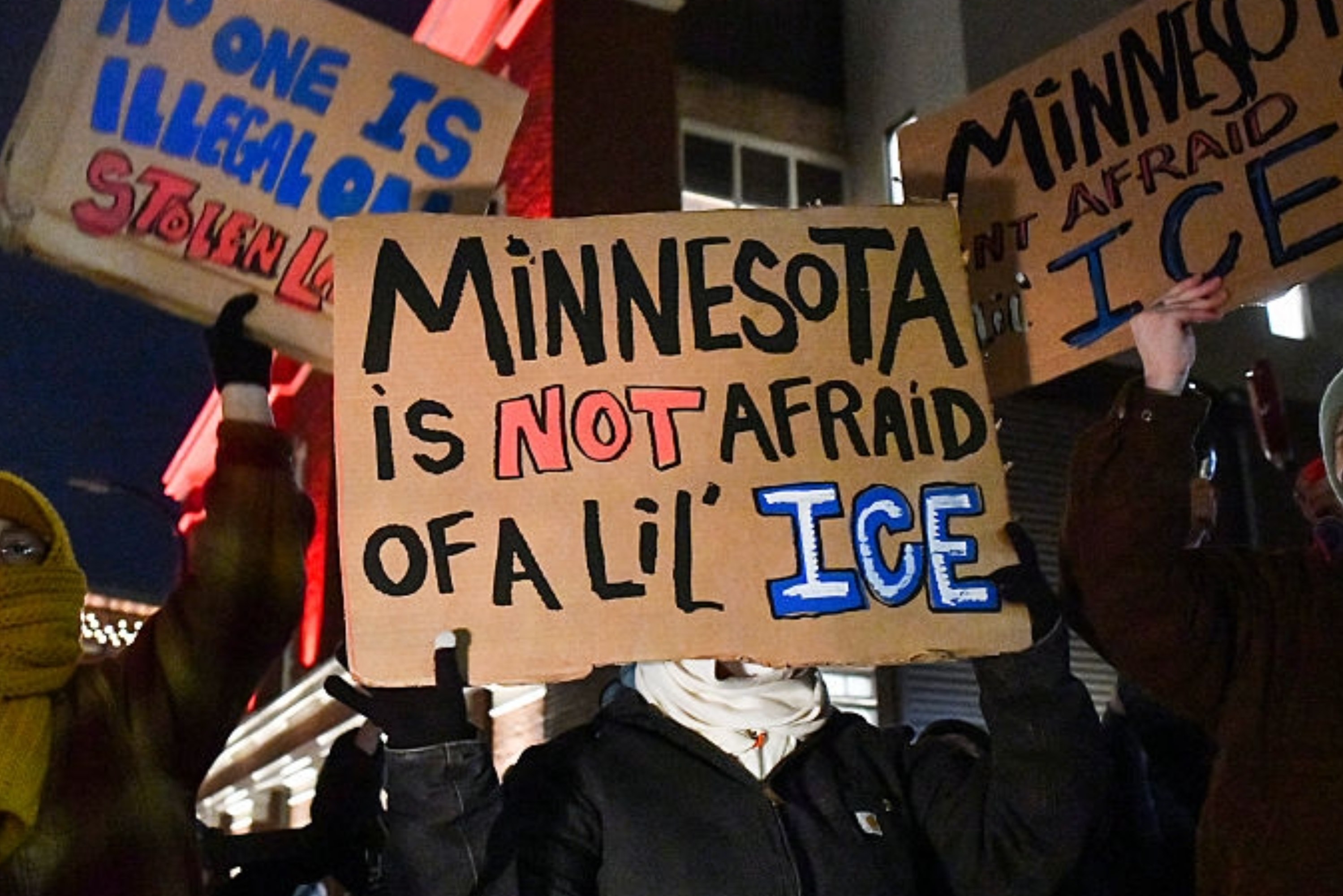 Demonstranter holder skilt med teksten «Minnesota er IKKE redd for en lil' ICE" og "Ingen er ulovlig på stjålet land" på en nattlig demonstrasjon