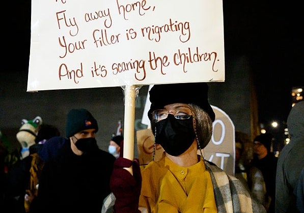 Demonstranten holder skilt som henvender seg til Kristi Noem på et nattlig rally, omgitt av andre. Sign kritiserer virkningen av Kristi Noems politikk