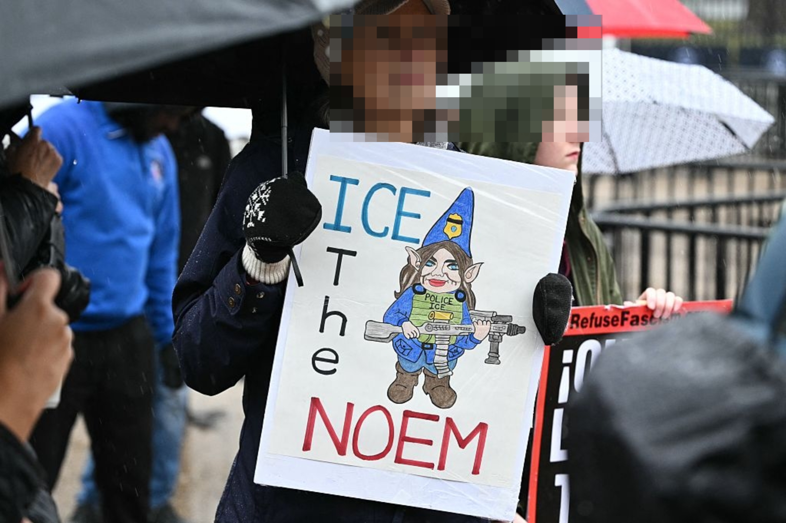 Personen holder et protestskilt med en tegneserie-nisse iført politihatt, holder en rifle, og teksten 