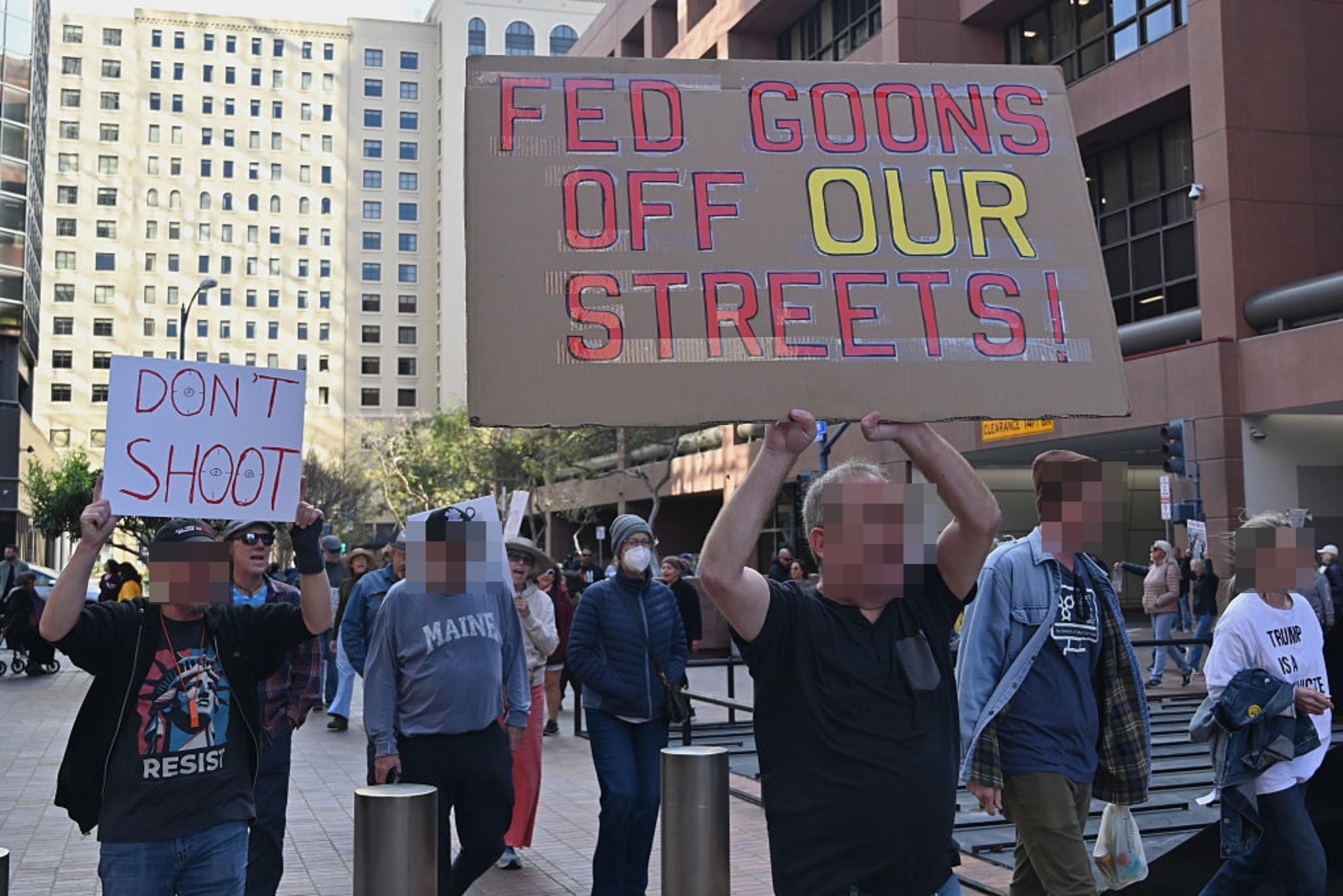 Folk protesterer i en by og holder skilt som sier «FED GOONS OFF OUR GATES!" og "IKKE SKYT" uttrykker motstand mot føderal tilstedeværelse