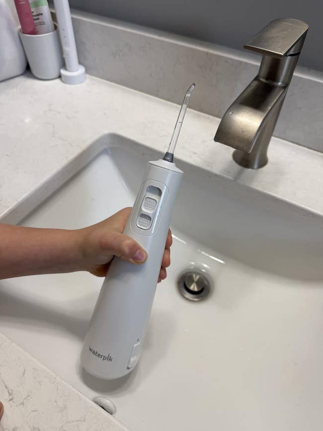 Person holding a Waterpik h2o  flosser implicit    a sink, showcasing the appliance's plan  and usability