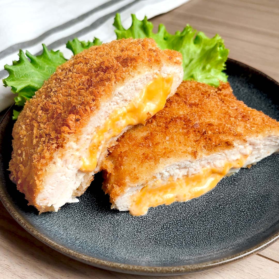 揚げたささみカツにとろけるチーズが挟まれた料理が皿に盛られている。背景に緑の葉が添えられている。