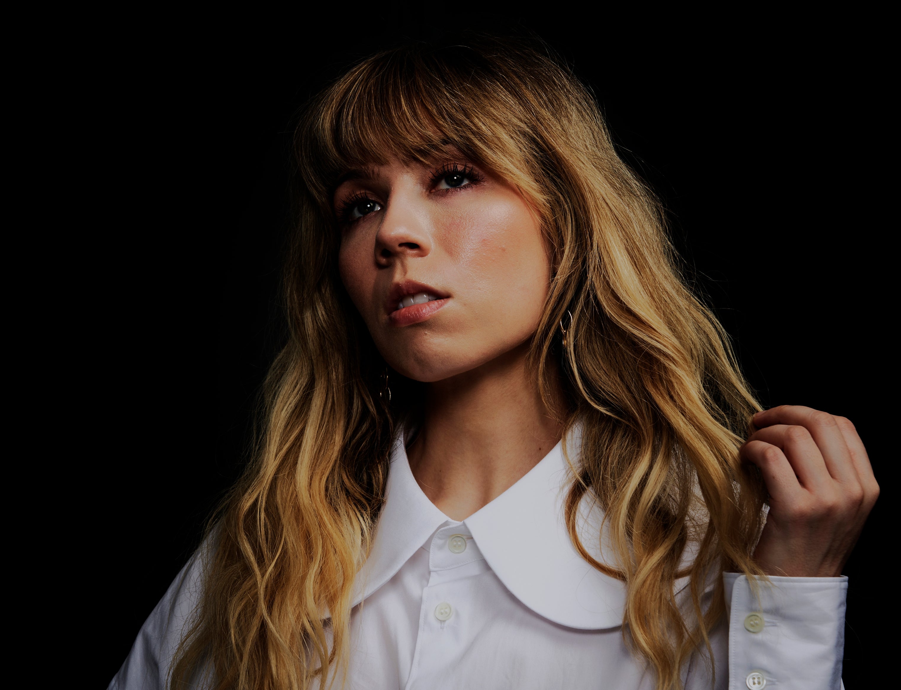 Person with long wavy hair wearing a wide-collared, long-sleeve shirt, gazing upwards in a thoughtful pose