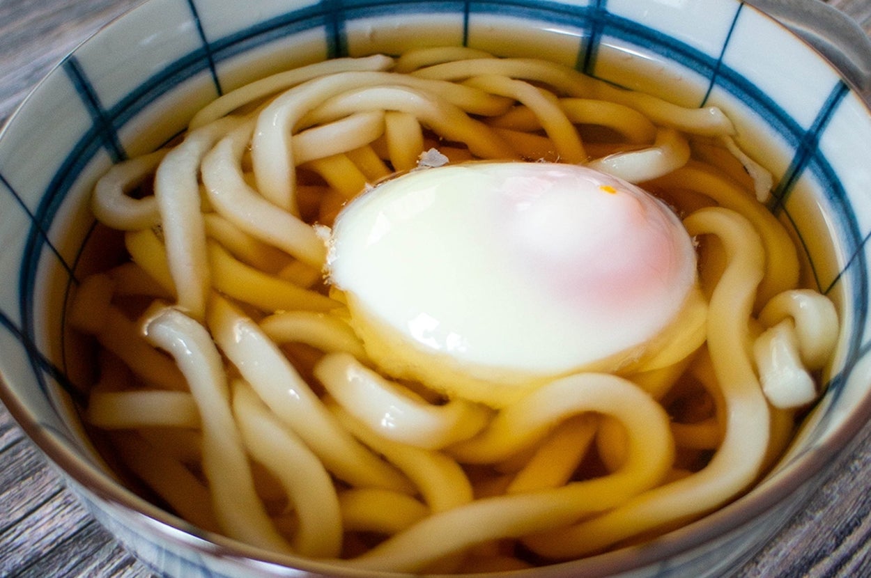 椀に盛られたうどんと半熟卵。スープが豊富で、温かい一品として仕上がっている。