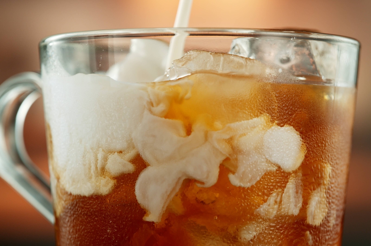 Close-up of iced coffee in a glass mug with milk being poured in, creating a swirling pattern