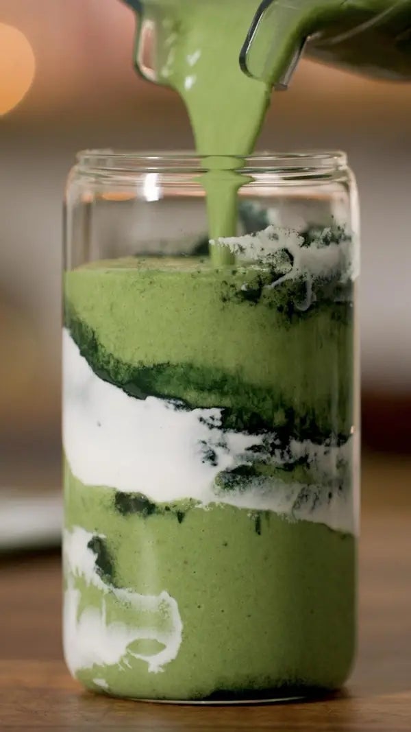 Green smoothie being poured into a glass jar with layered white yogurt