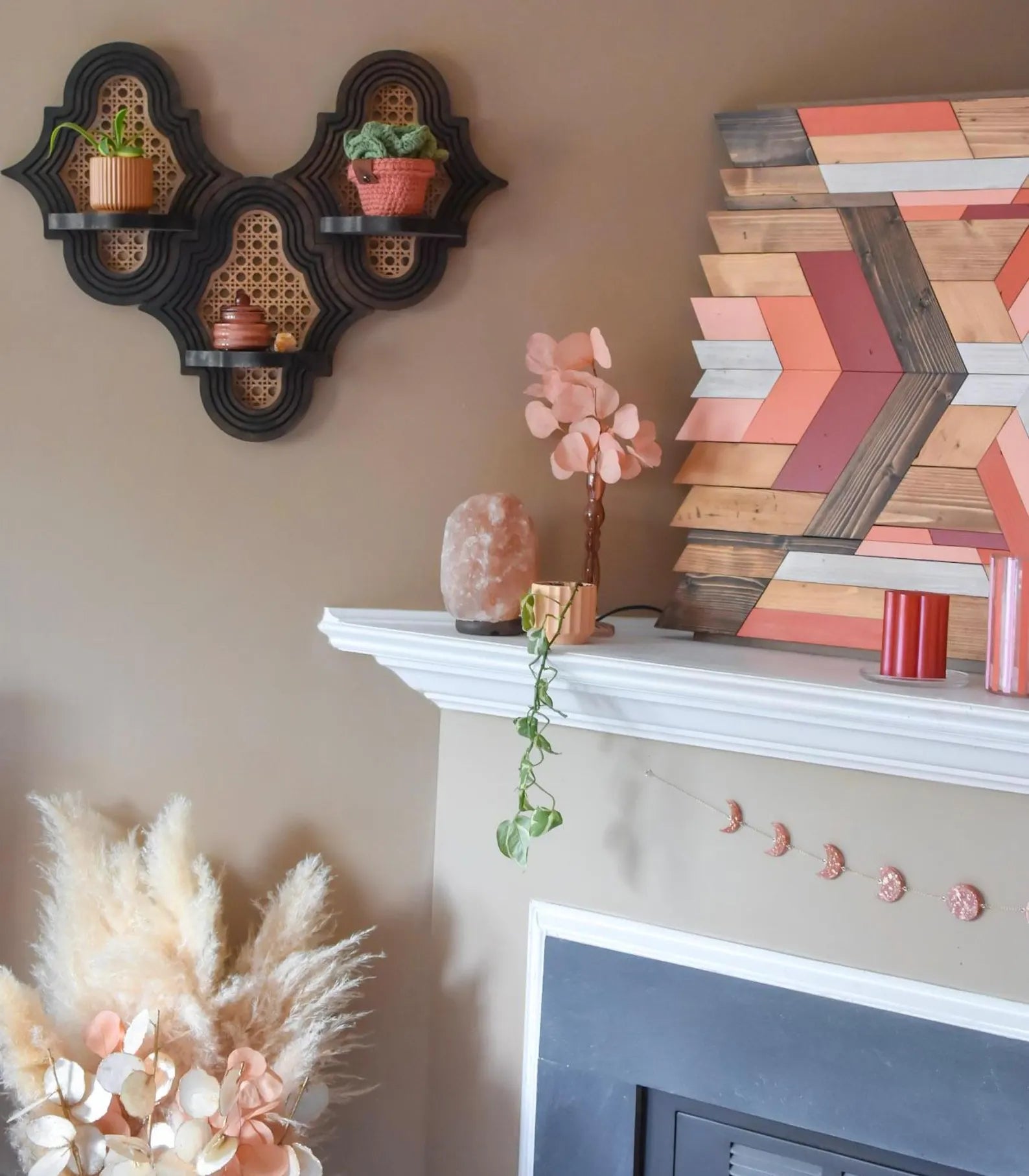 Home decor mounting  featuring a modern   partition  support  with plants, a geometric wood   creation  piece, and a mantel adorned with candles and pampas grass
