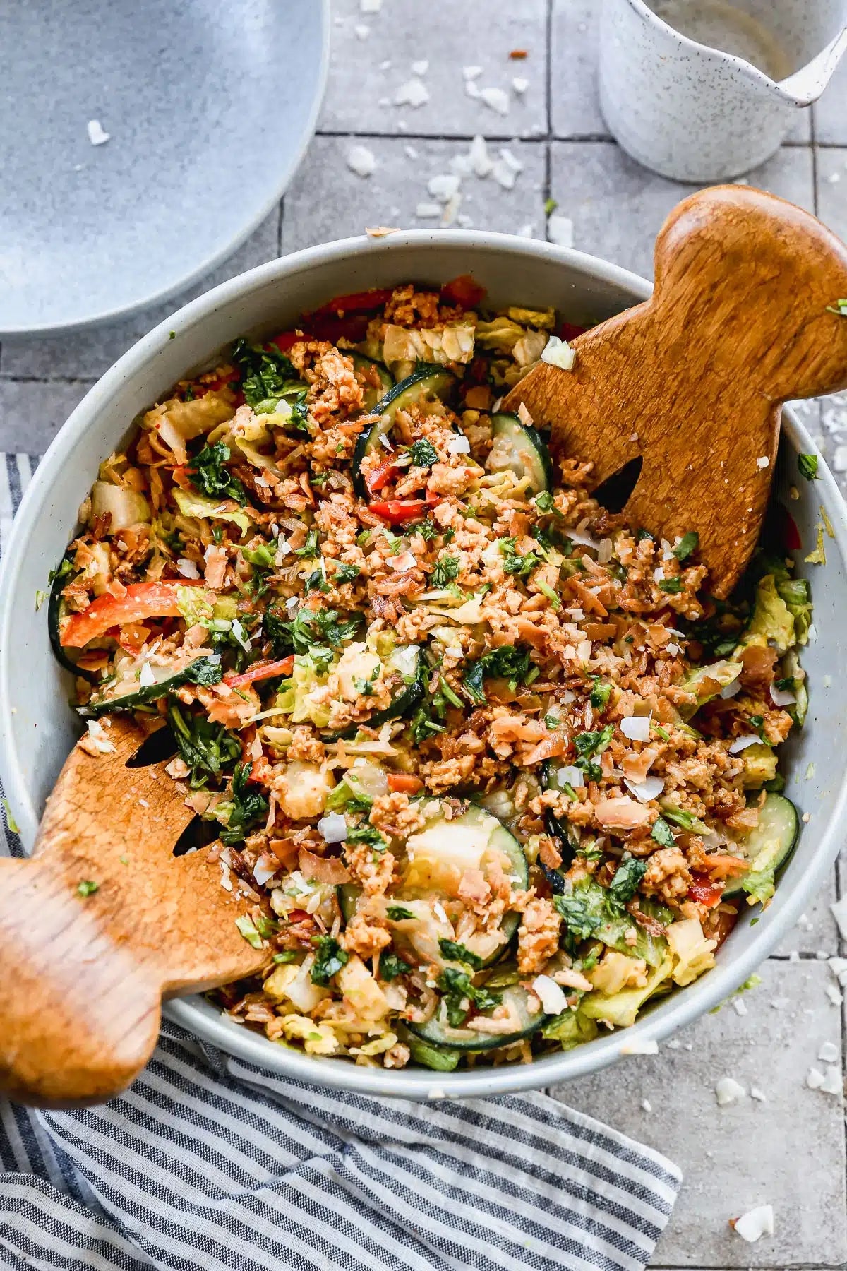 Bowl of mixed salad with cucumbers, tomatoes, and quinoa, topped with fresh herbs and served with wooden salad servers
