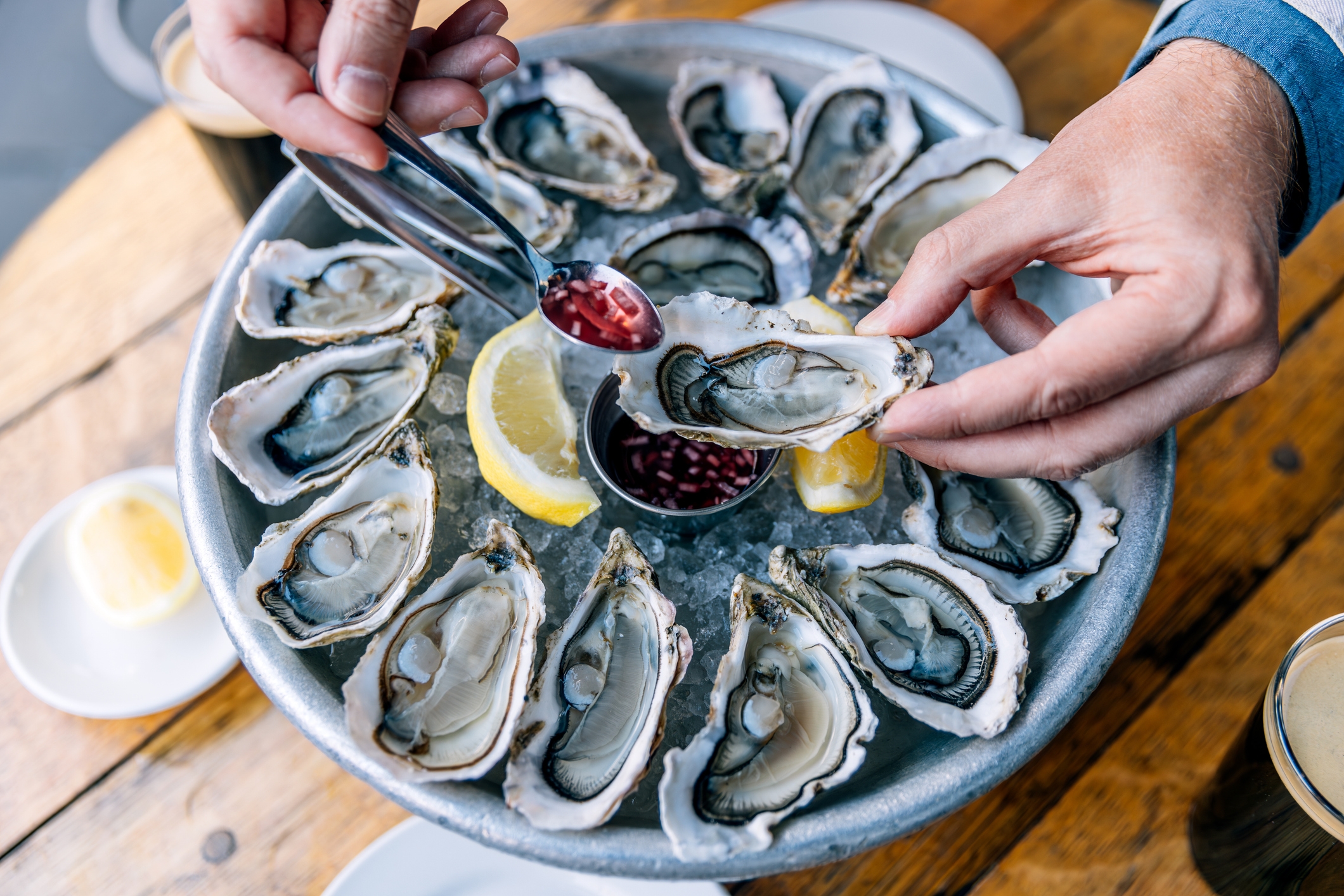 A person prepares to eat fresh oysters from a platter, adding sauce with a spoon, enhancing a romantic dining experience