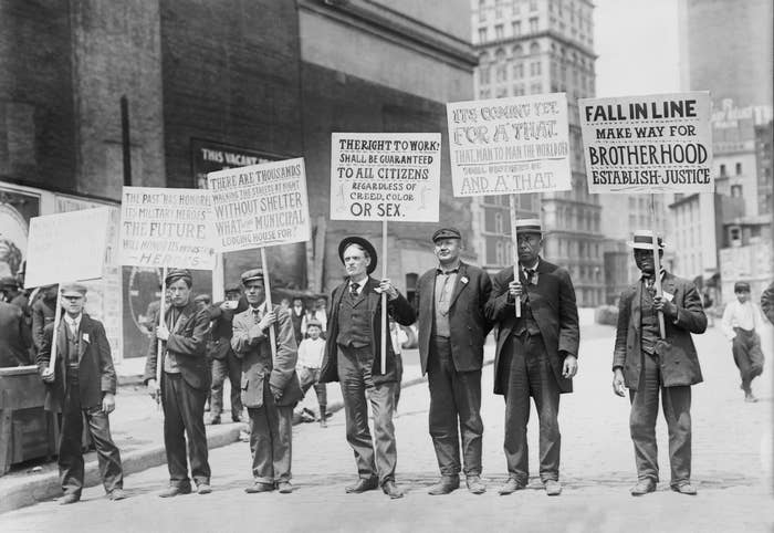 A radical  of men successful  suits holding signs advocating for employment   rights and societal  justness  successful  an aboriginal  20th-century municipality  setting
