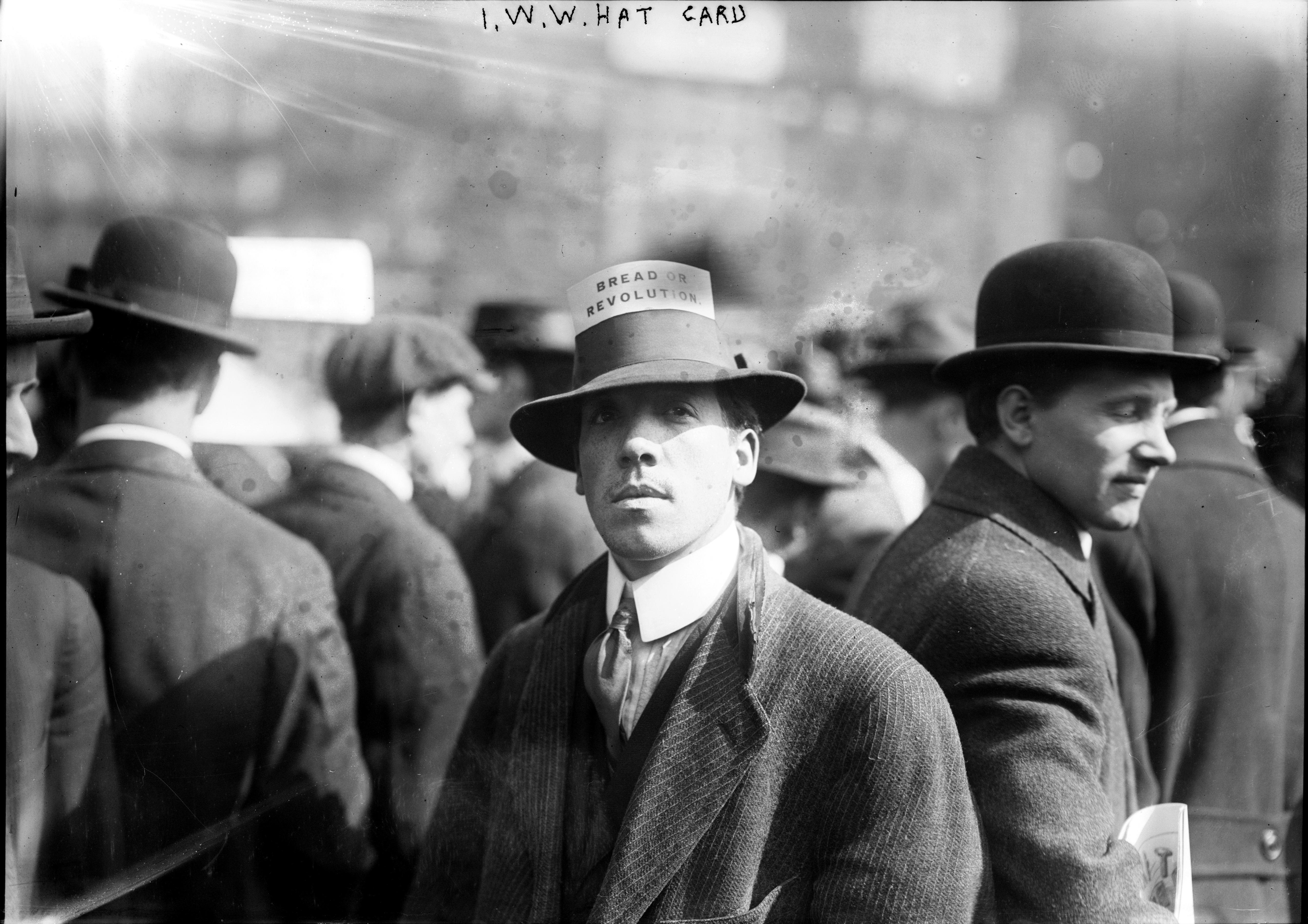Man successful  aboriginal  20th-century attire stands with others. His chapeau  features a "Break The Revolution" card