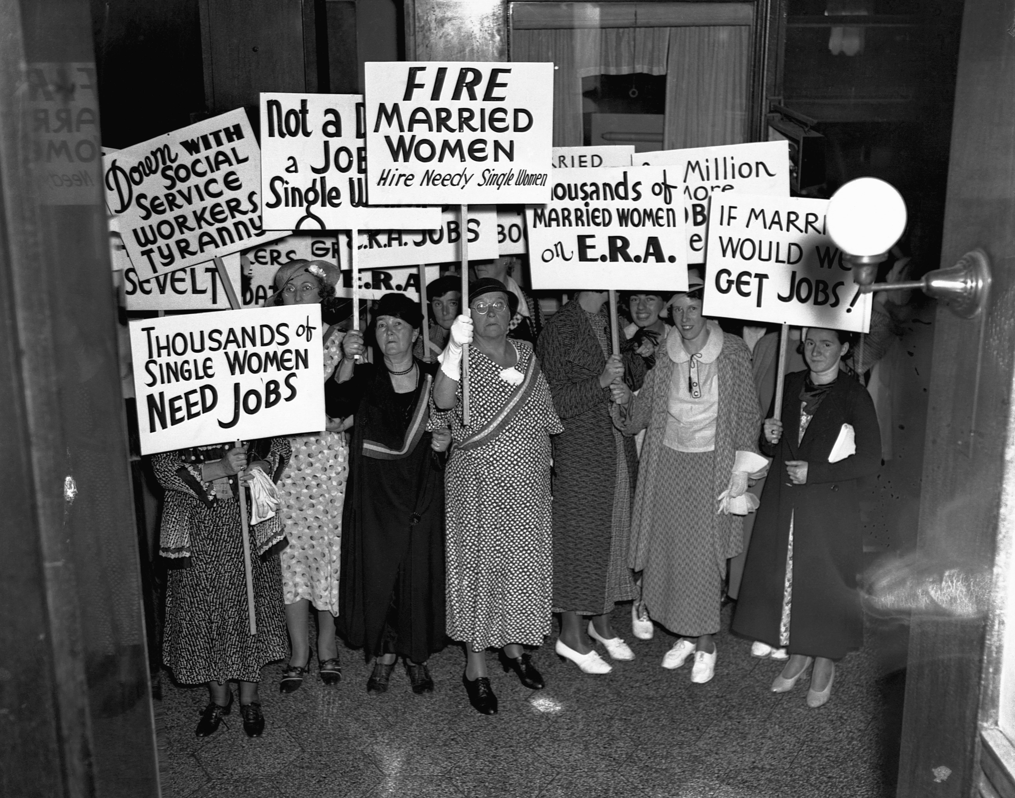 A radical  of women protestation  successful  1930s attire, holding signs demanding jobs for azygous  women, opposing employment   of joined  women during the Great Depression