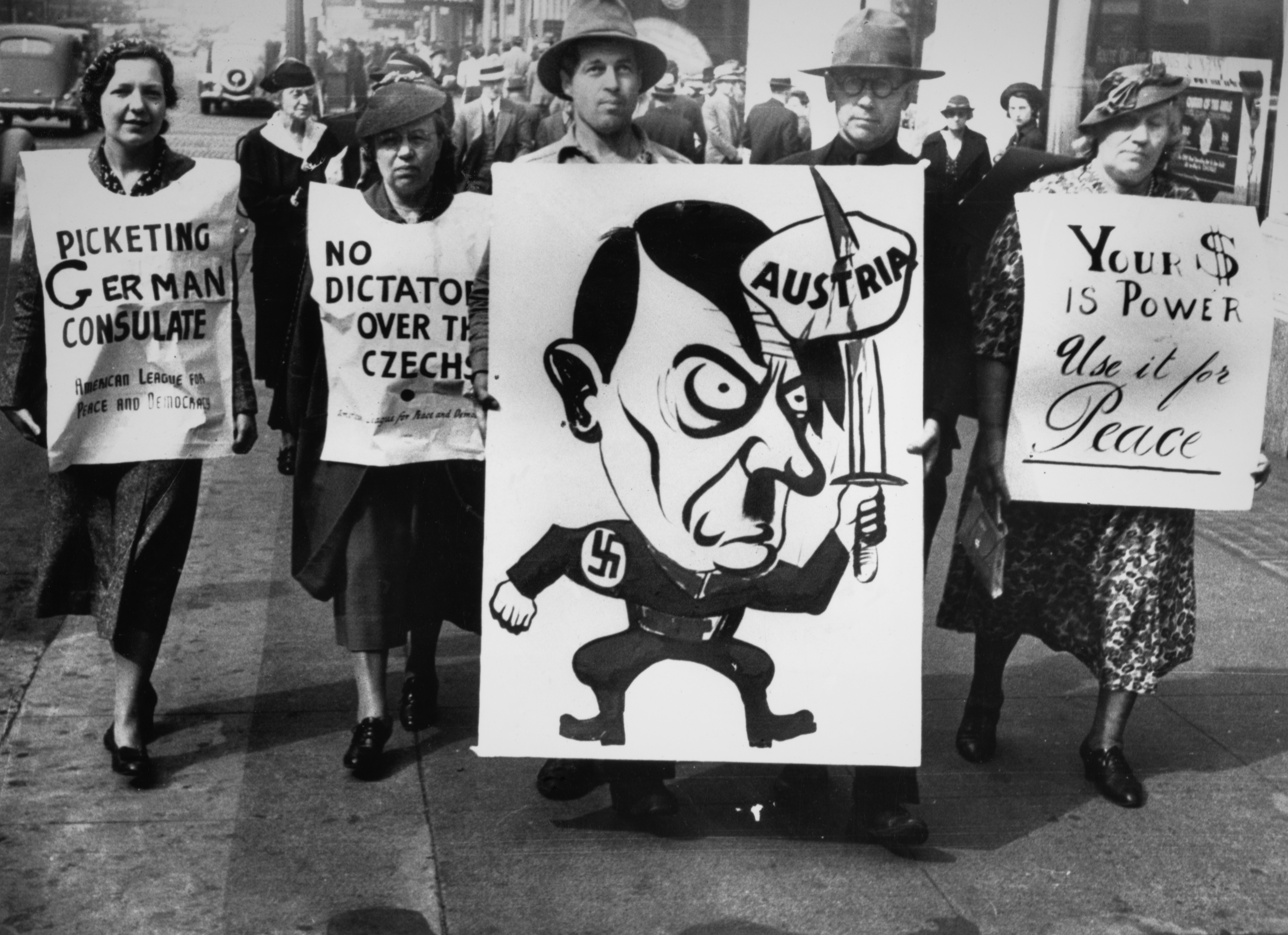 Protesters clasp  anti-Nazi signs, including a caricature of Hitler, during a demonstration. Signs telephone  for enactment   against Germany's expansion