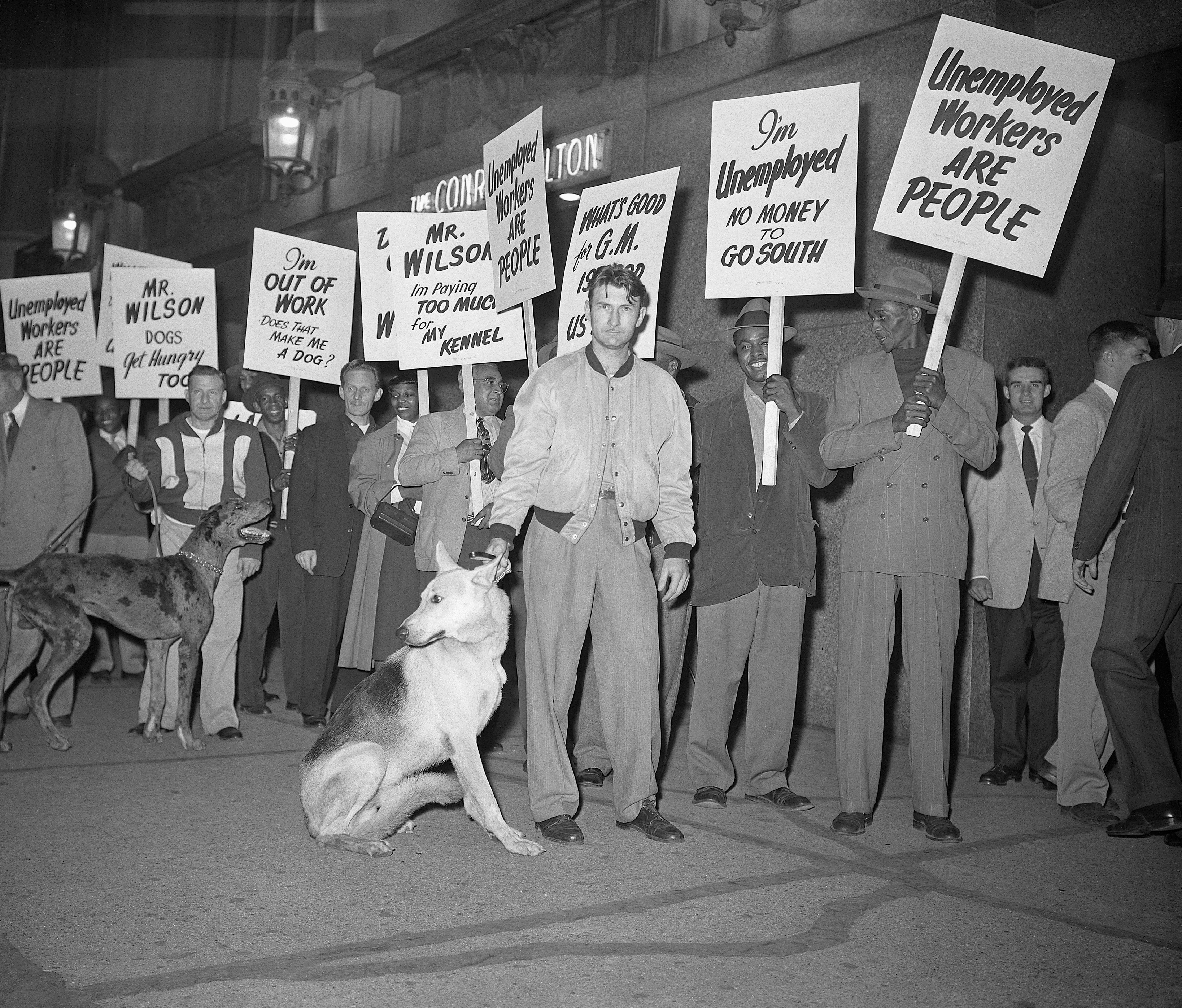 People clasp  signs demanding jobs and fairness successful  an unemployment protest. A canine  sits adjacent   the protesters
