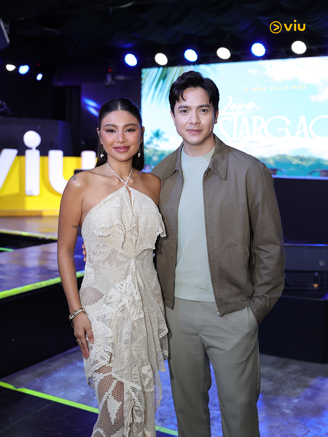 Two people posing in stylish attire at a media event, with a Viu backdrop