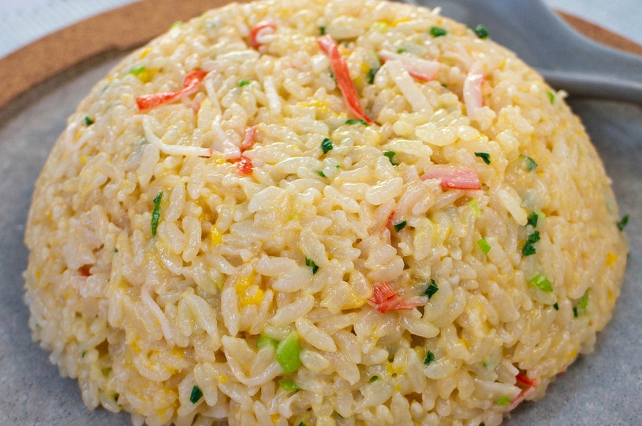 皿に盛られたチャーハンがテーブルに置かれ、スプーンが添えられています。色とりどりの具材が混ざっています。