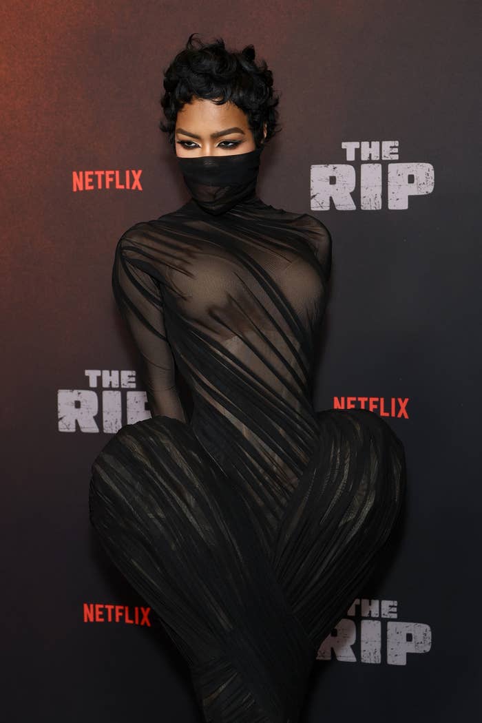 Person posing connected  reddish  carpet successful  a form-fitting, striped, sheer formal  with a look   covering, astatine  a Netflix lawsuit   backdrop