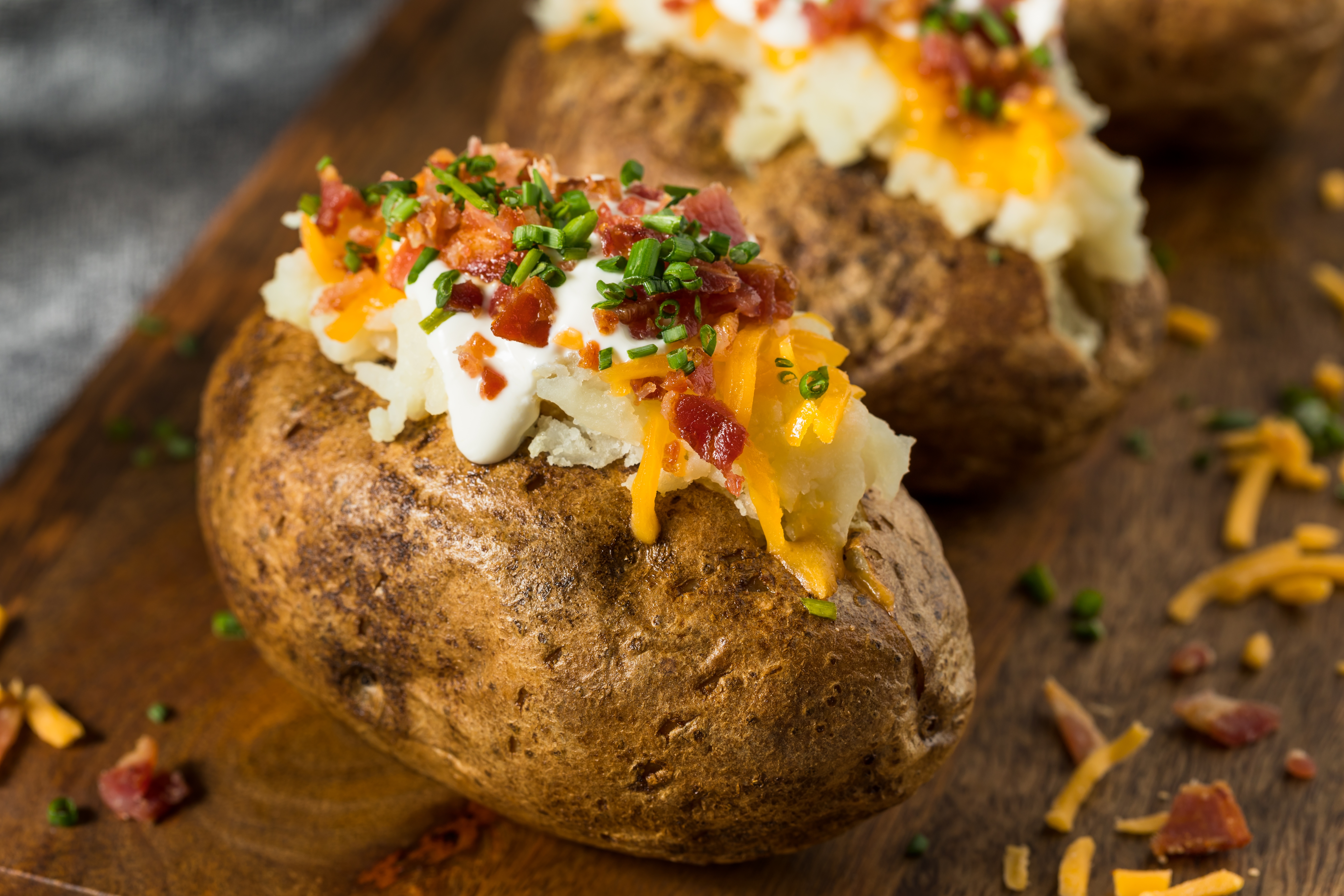 Loaded baked potatoes topped with sour cream, cheese, bacon, and chives on a wooden board