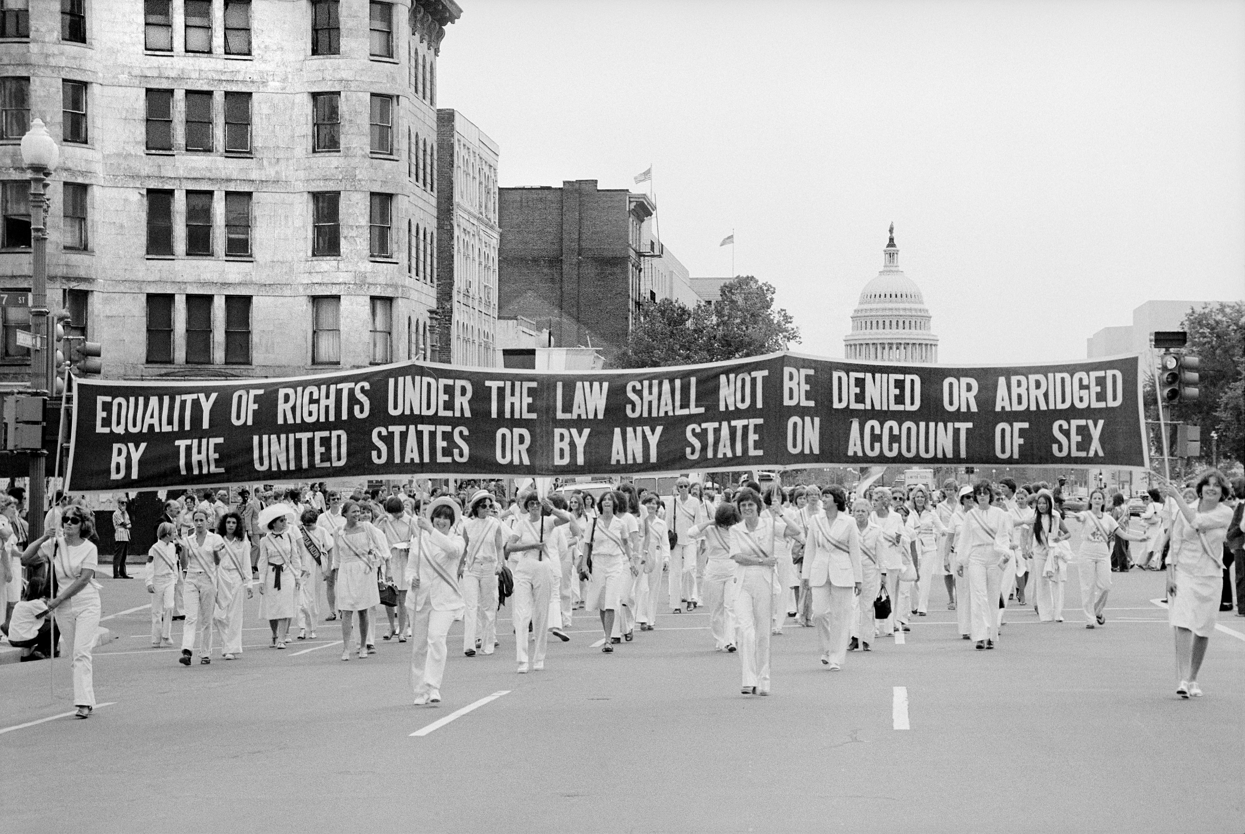 A radical  of women marches with a banner advocating for adjacent   rights nether  the law, featuring the U.S. Capitol successful  the background