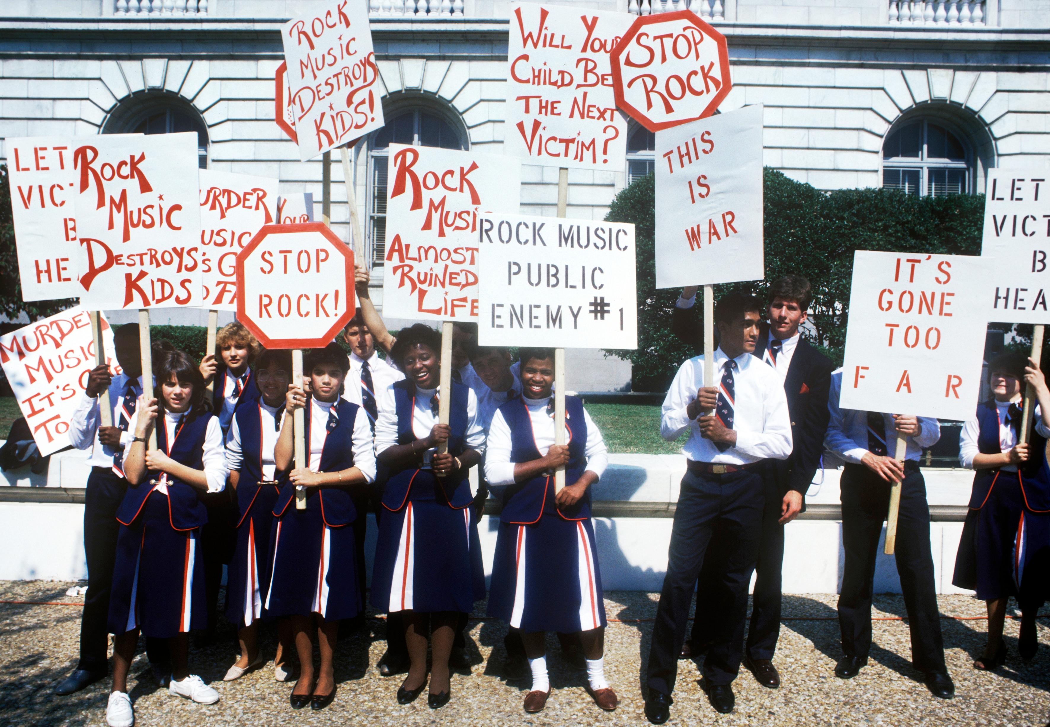 People successful  coordinated outfits clasp  protestation  signs against stone  music, saying phrases similar  "Stop Rock" and "Rock Music Destroys Kids' Minds."