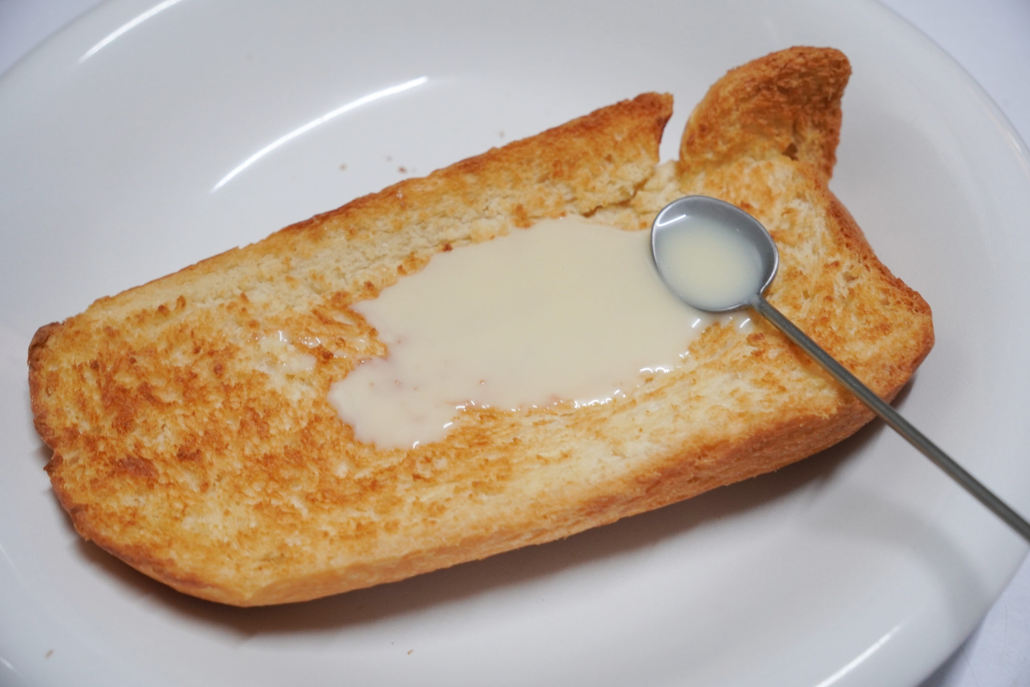 Toasted bread slice drizzled with condensed milk on a white plate