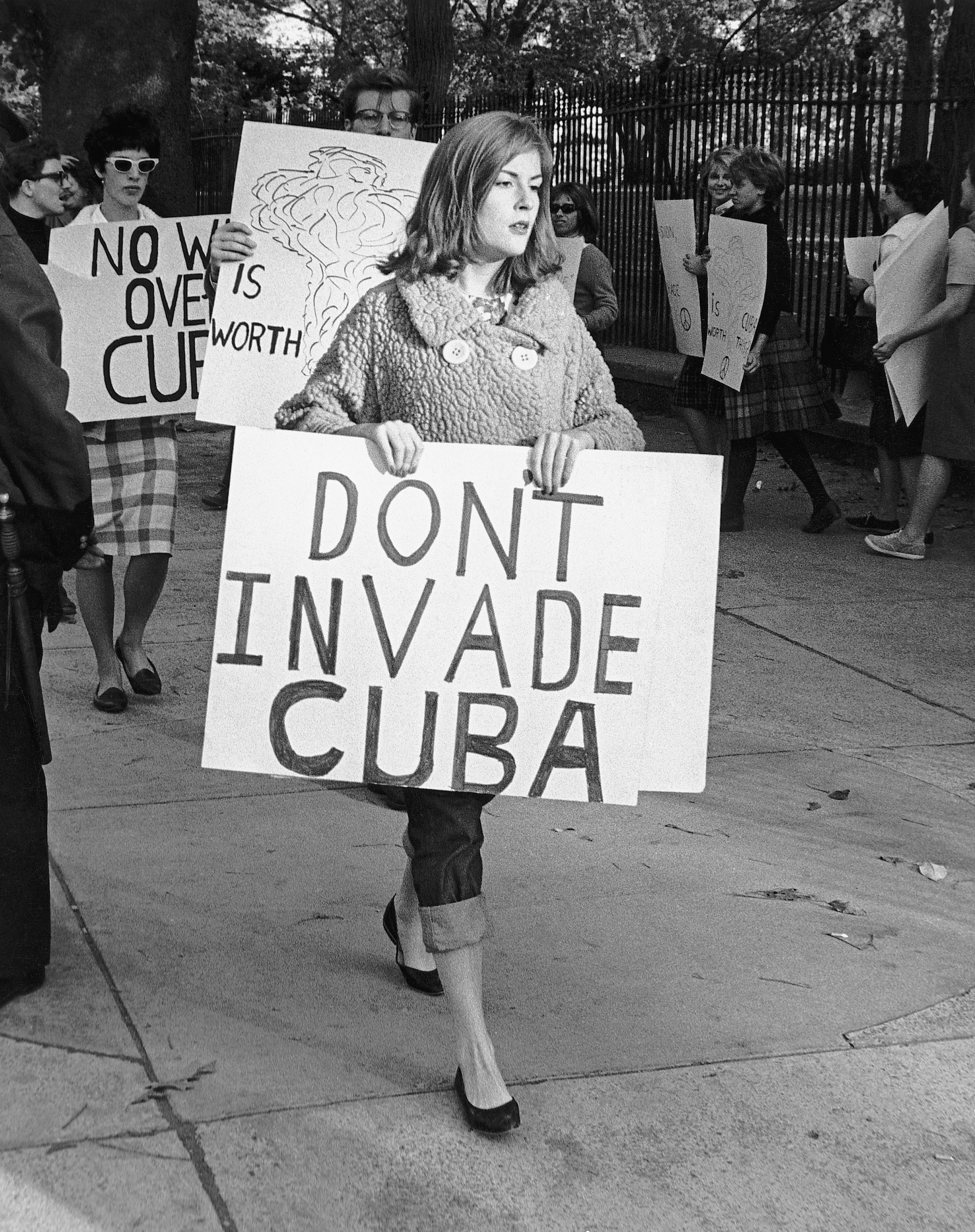 Woman marches successful  protestation  holding "DON'T INVADE CUBA" sign, surrounded by others with antithetic  protestation  signs