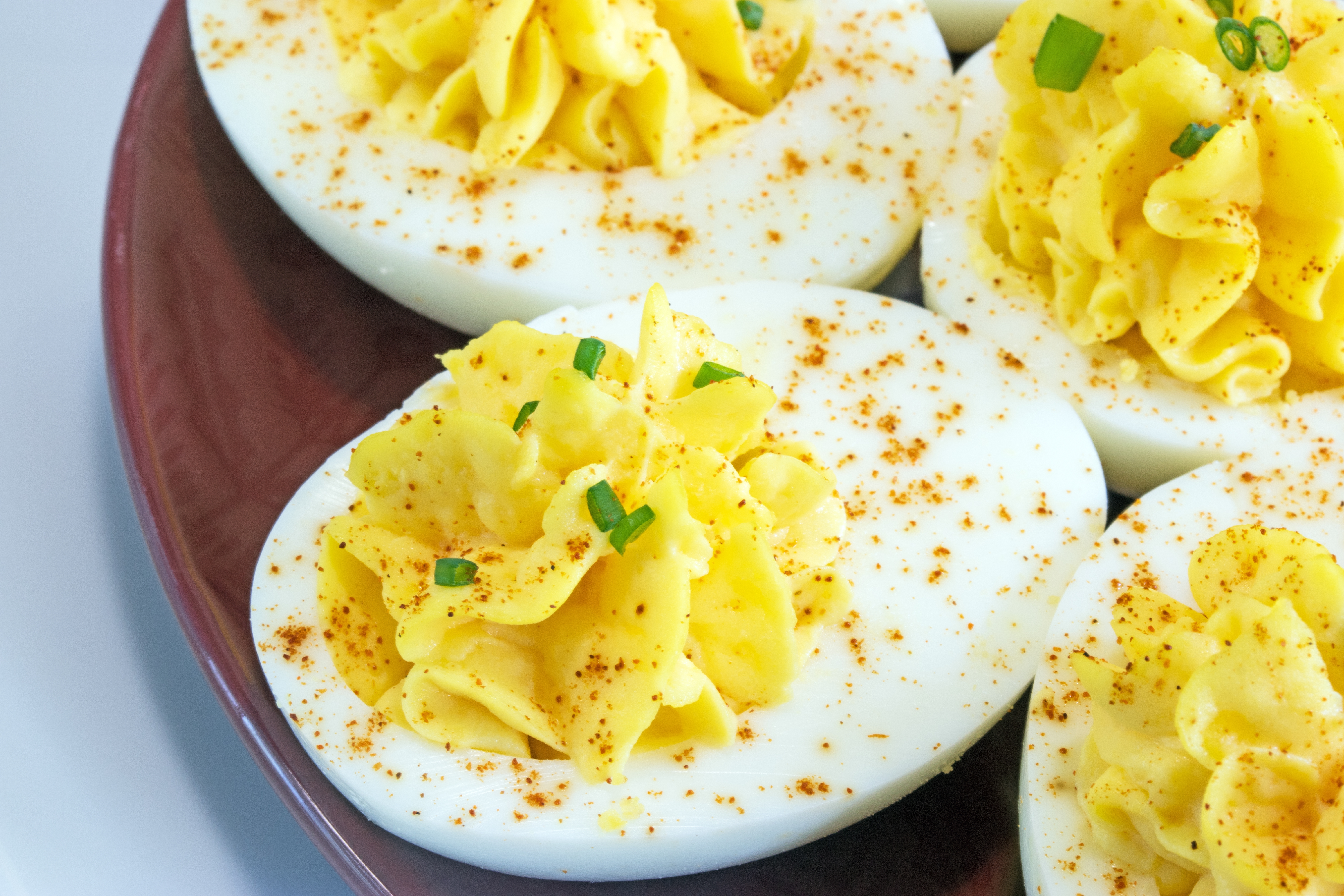 Plate of deviled eggs garnished with chives and paprika, arranged neatly on a dark dish