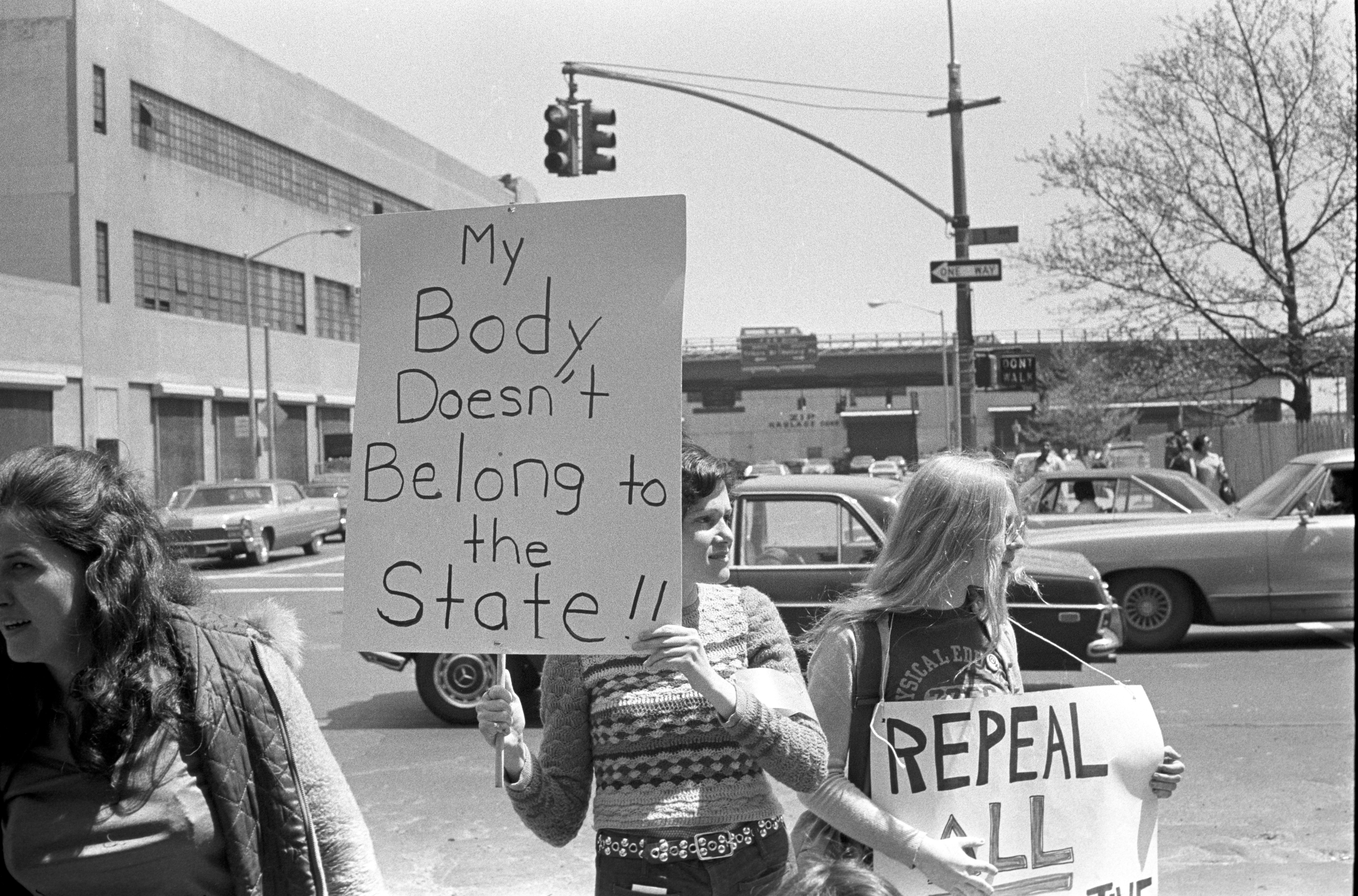 People clasp  protestation  signs connected  a street, including "My Body Doesn't Belong to the State!!" and "Repeal All" successful  a black-and-white photo