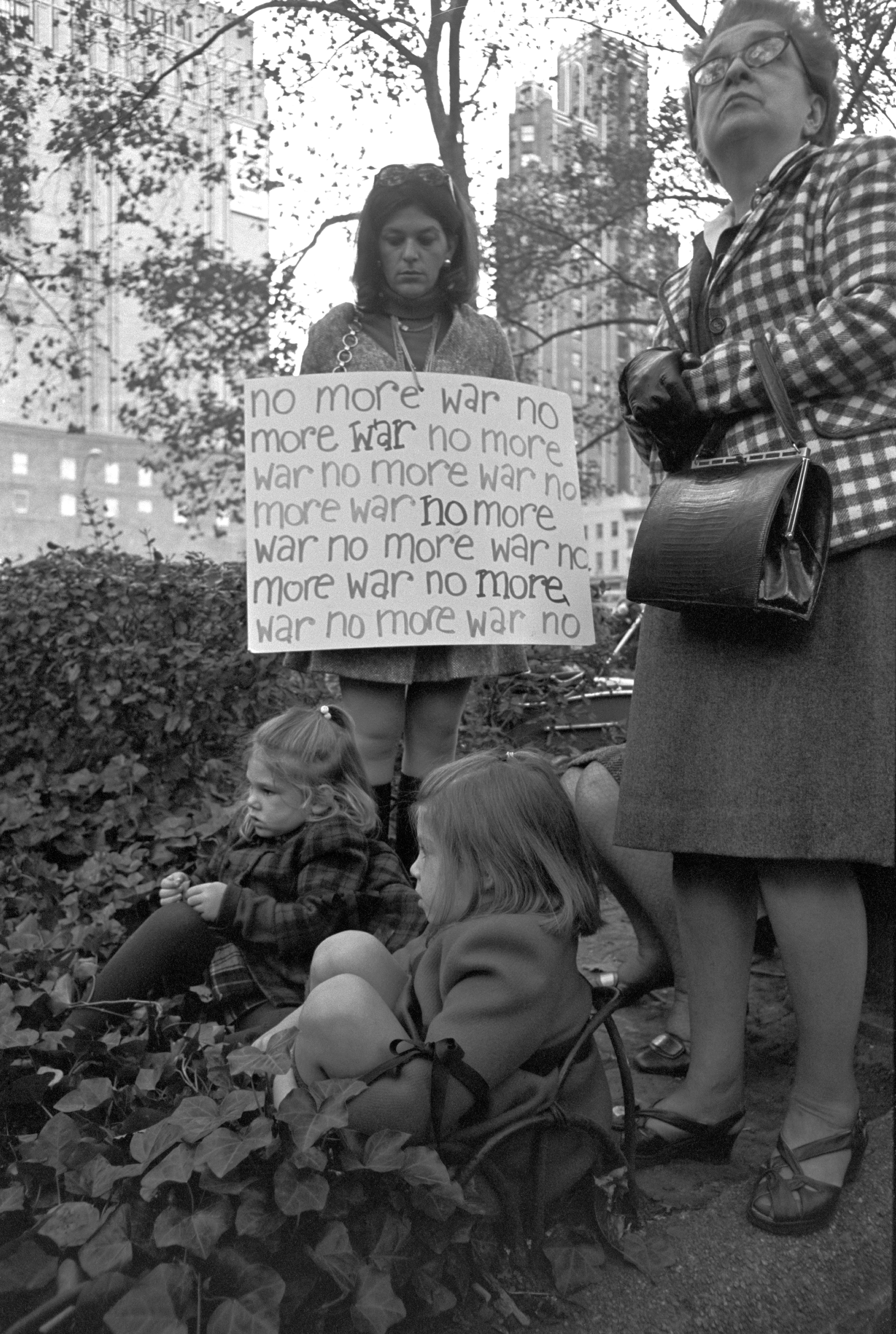 A radical  of radical   protestation  successful  a parkland  holding a motion   speechmaking  "no much  war" repeatedly, surrounded by 2  children sitting connected  the ground