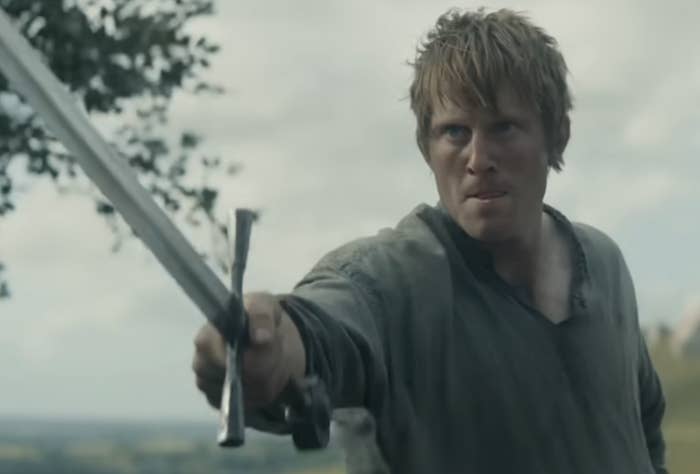 A person holding a sword looks determined in a historical drama scene, standing outdoors in expansive countryside. Subtitles say, "To defend the weak."