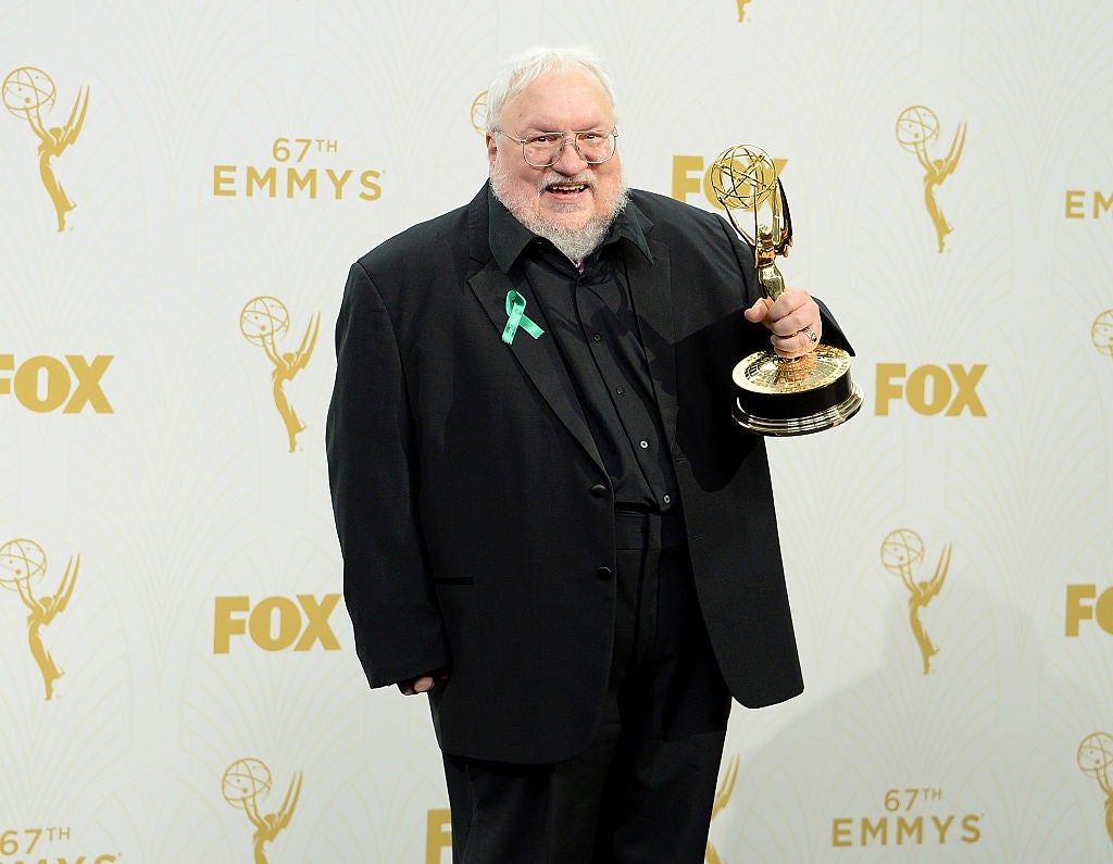 Person holding an Emmy award, wearing a black suit with a green ribbon, standing in front of a backdrop with Emmy branding at the 67th Emmy Awards