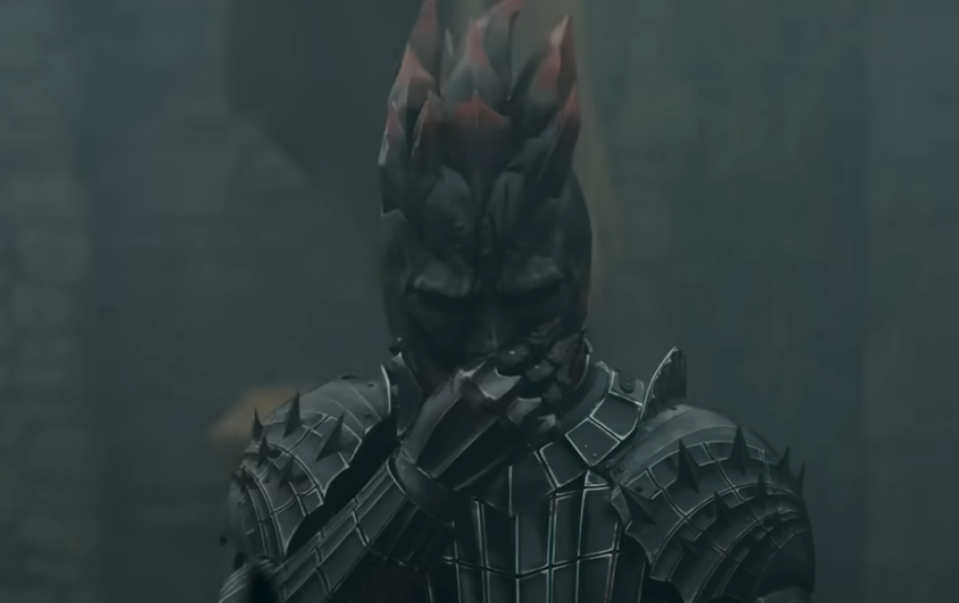 Person in detailed armor holds hand to face in a dramatic scene, suggesting a tense or contemplative moment from a TV show or movie