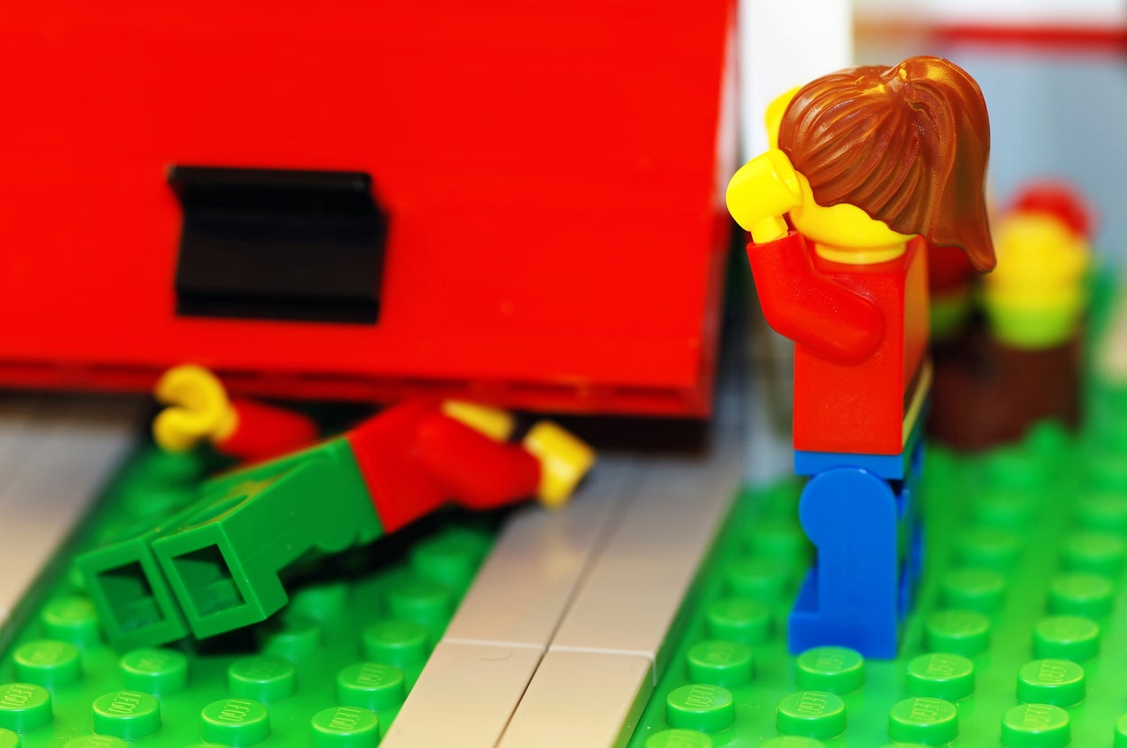 Two LEGO figures with one looking distressed near a fallen figure under a LEGO structure
