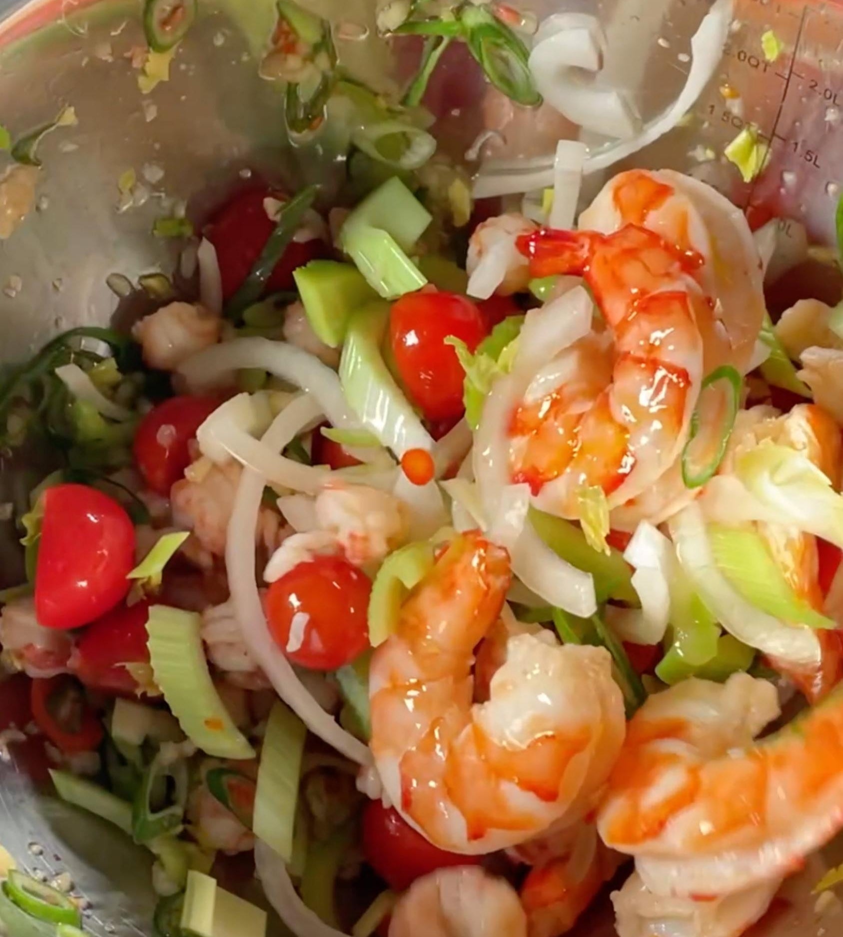 A bowl of fresh shrimp salad with chopped vegetables and cherry tomatoes, garnished with green onions