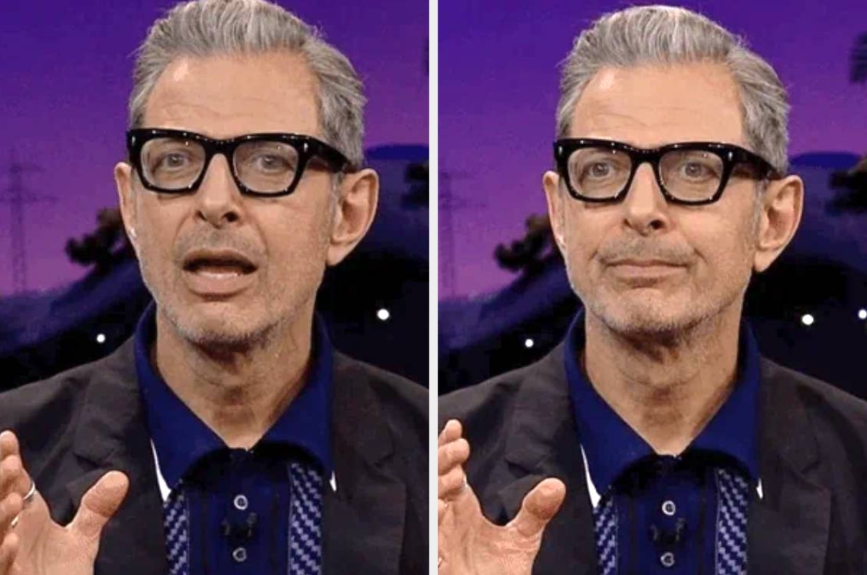 A man with gray hair and glasses speaking expressively on a talk show set, wearing a blazer over a polo shirt