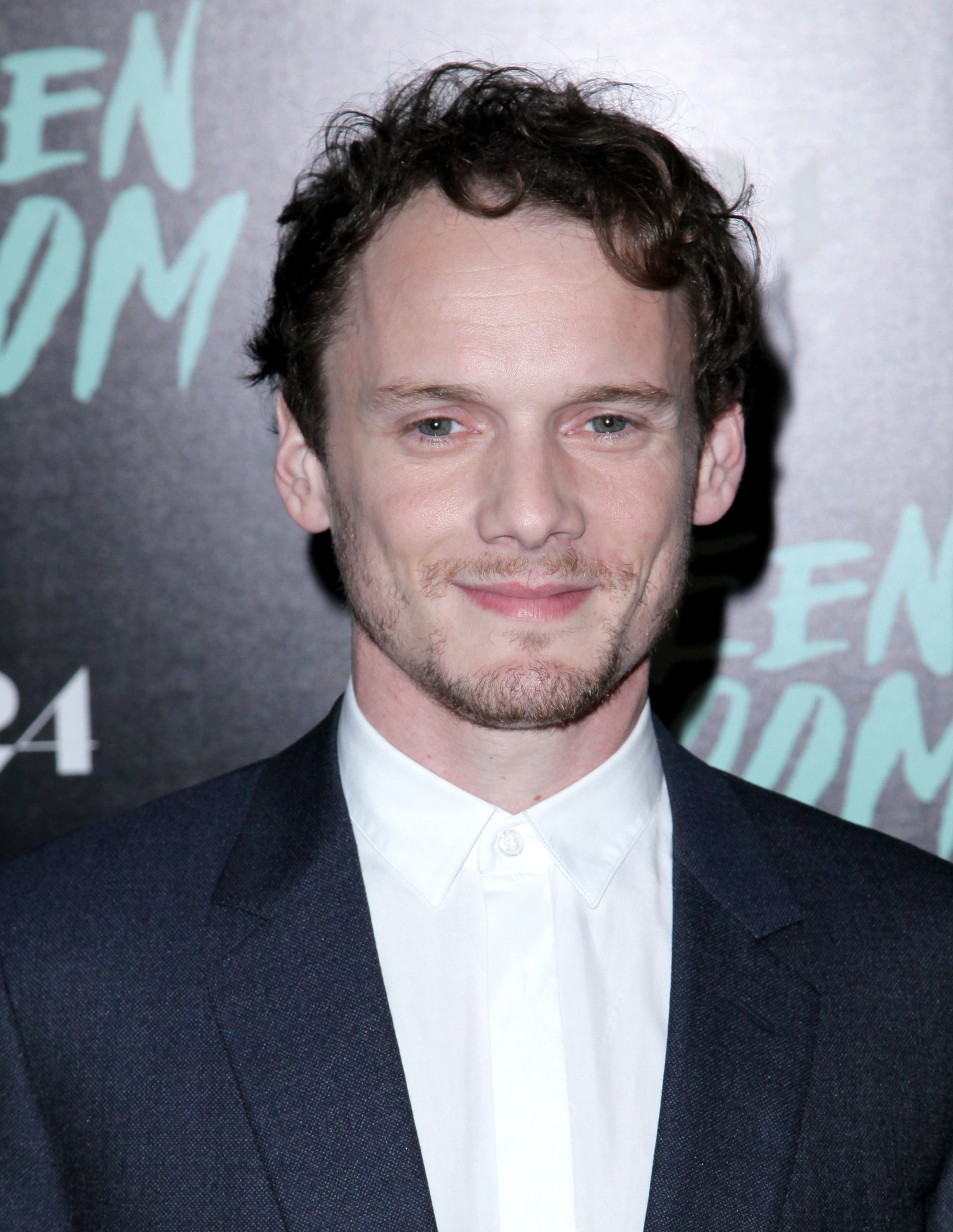 A person in a suit and white shirt at a film premiere, standing in front of a backdrop with the words "Green Room."