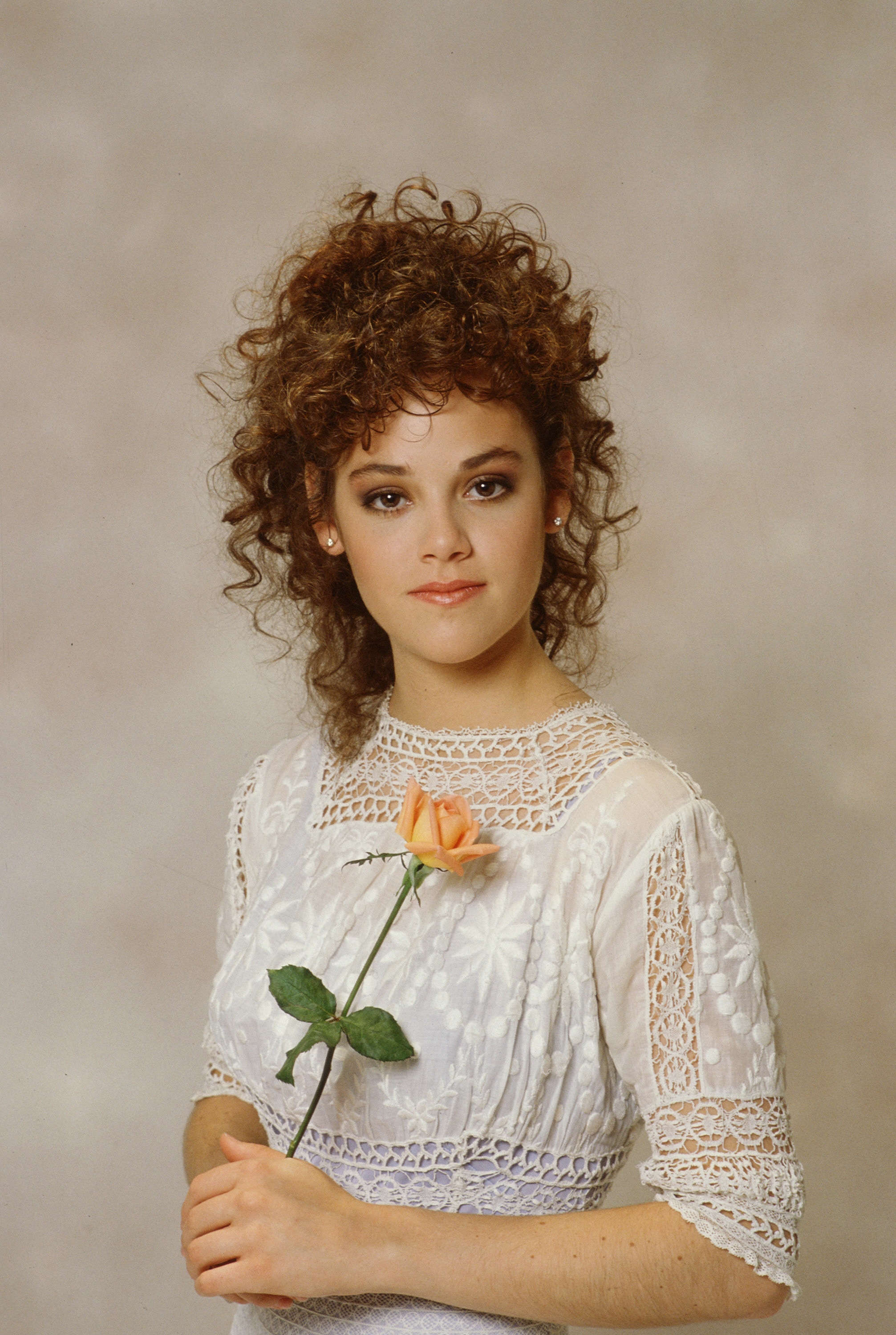 Woman with curly hair in a lace dress holding a rose, posing for a studio portrait
