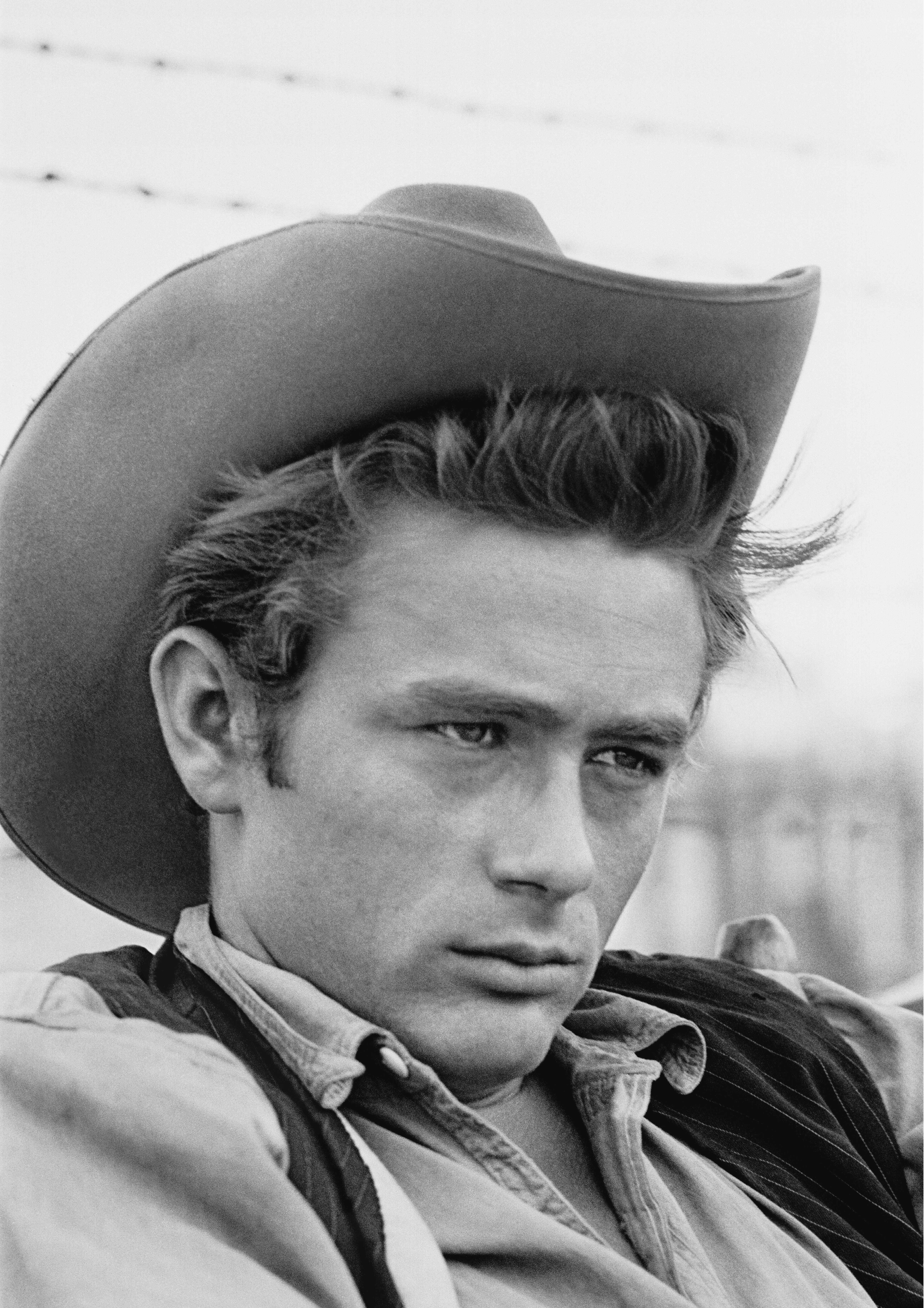 A person wearing a cowboy hat and a collared shirt gazes thoughtfully into the distance