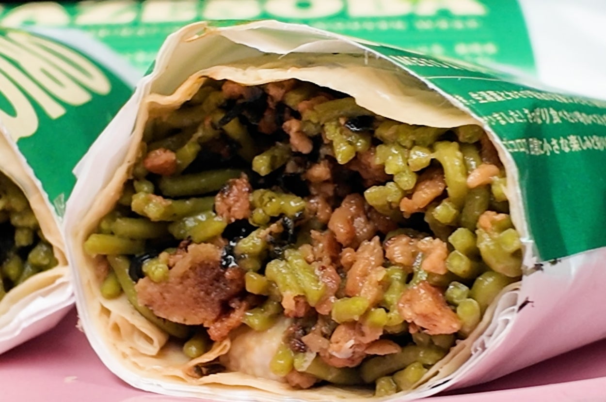 緑のパッケージに包まれたライスと具材の入ったブリトー。ピンクの皿に載っている。