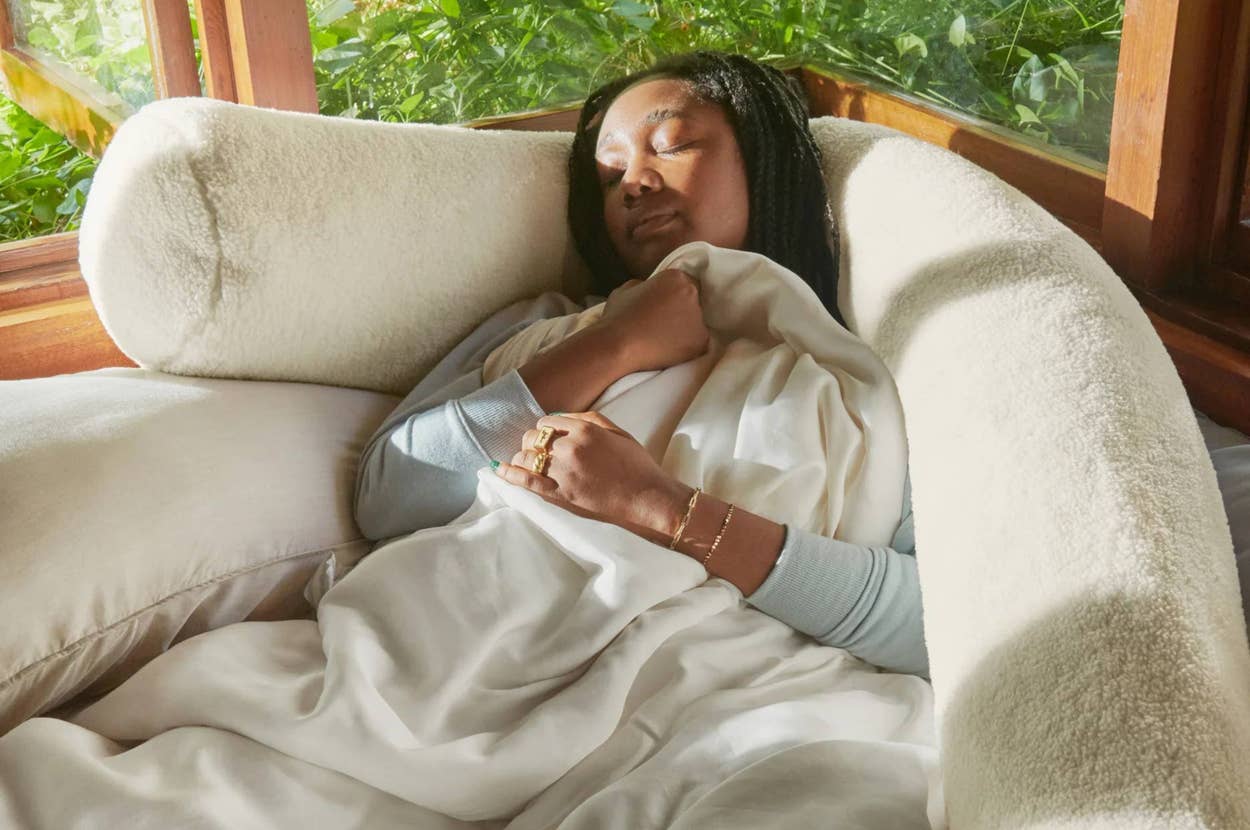 Person resting comfortably in a plush, cozy setting, wrapped in soft bedding. They appear relaxed and content in a peaceful environment