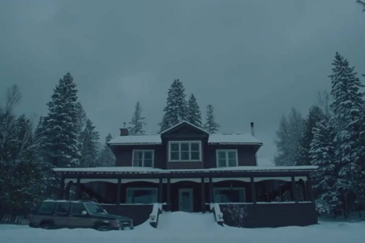 A large house with snow-covered surroundings and evergreen trees; a vehicle is parked beside the home. The scene suggests a cold, wintry setting