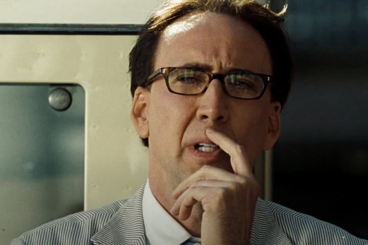 Nicolas Cage in "National Treasure: Book of Secrets" wearing glasses and a striped suit, thoughtfully looking ahead with a hand on his face