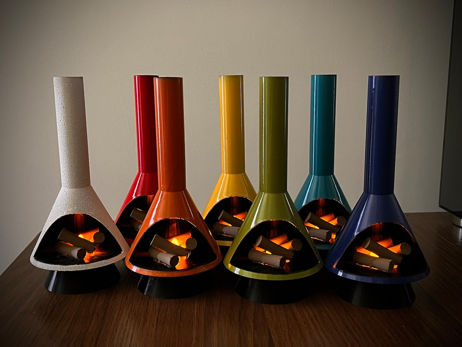 A collection of small, decorative tabletop fireplaces in various shapes and vibrant finishes displayed on a wooden surface