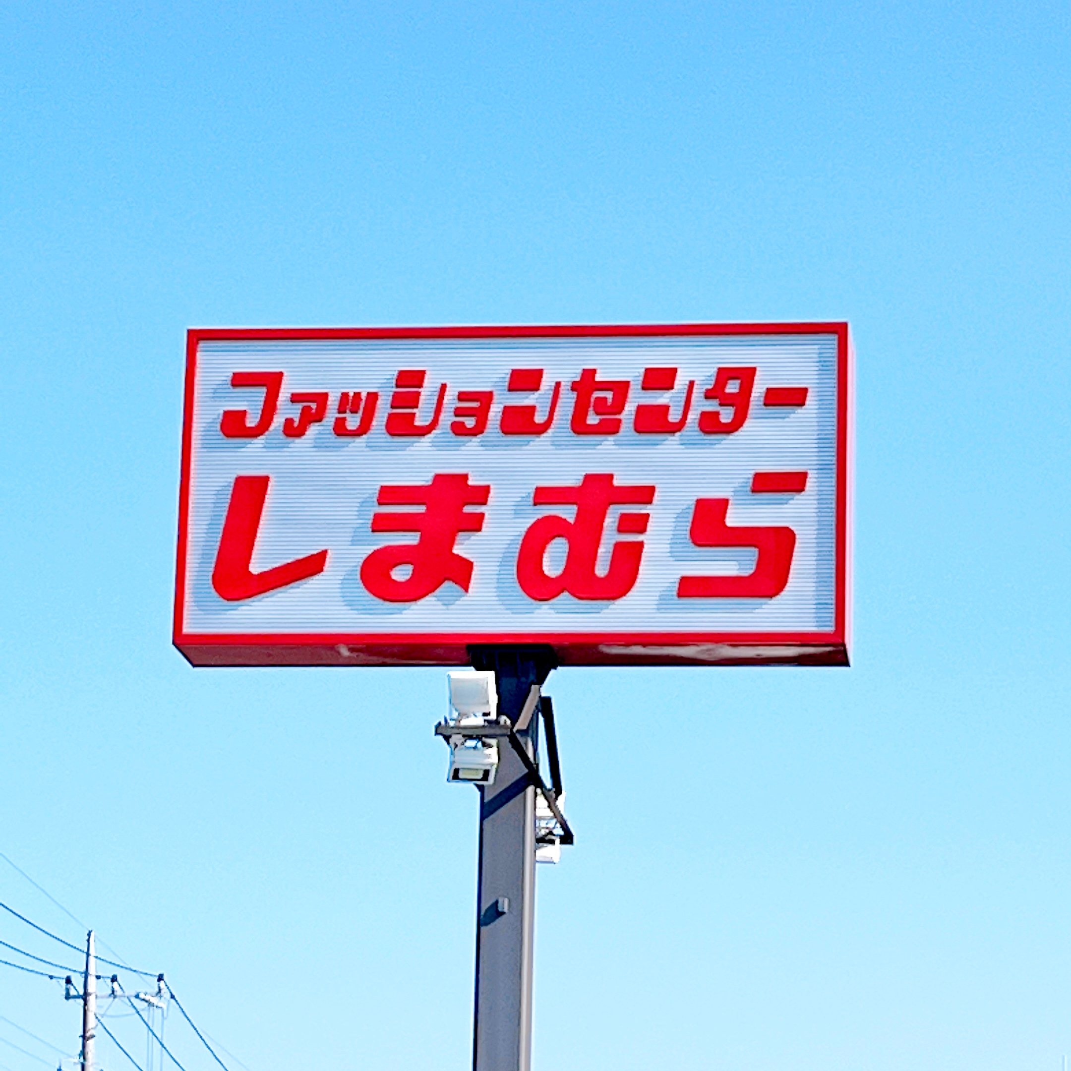 A tall sign with Japanese text on a pole against a clear sky