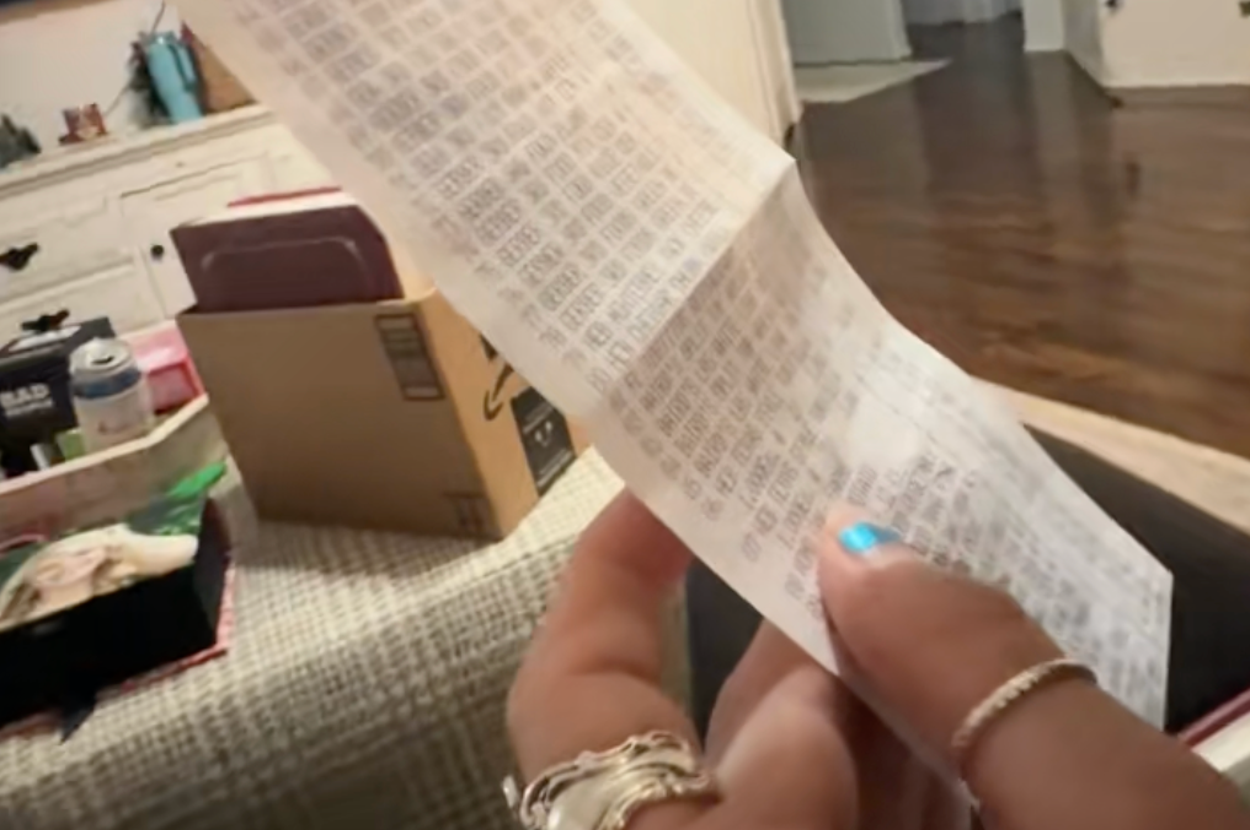 人物が長いレシートを手に持っている。背景に部屋の一部が見える。