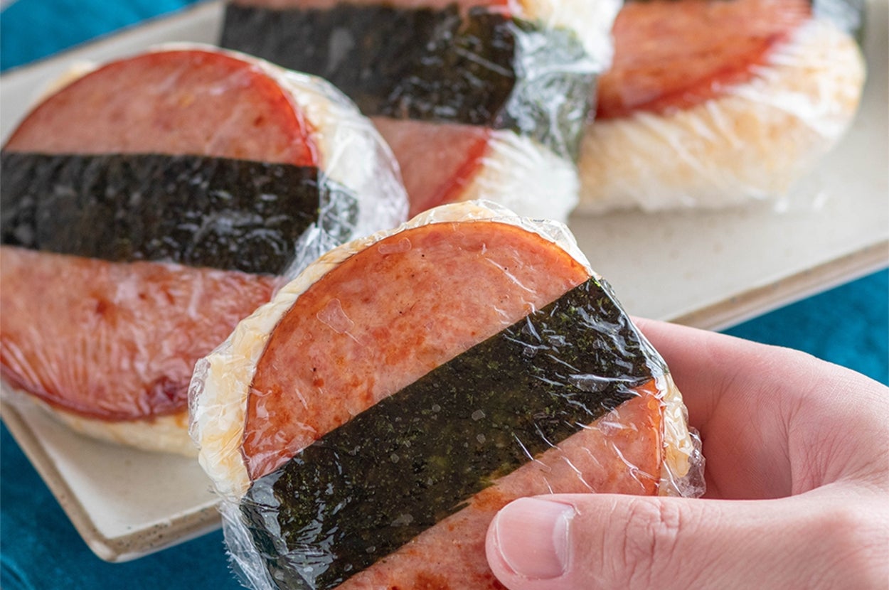 ランチョンミートと海苔を使ったスパムむすびが皿に並べられており、手に1つ持たれている。
