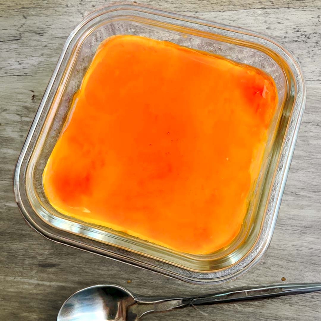 ガラス容器に入ったキャラメルソースがかかったプリンとスプーンがテーブル上に置かれている。